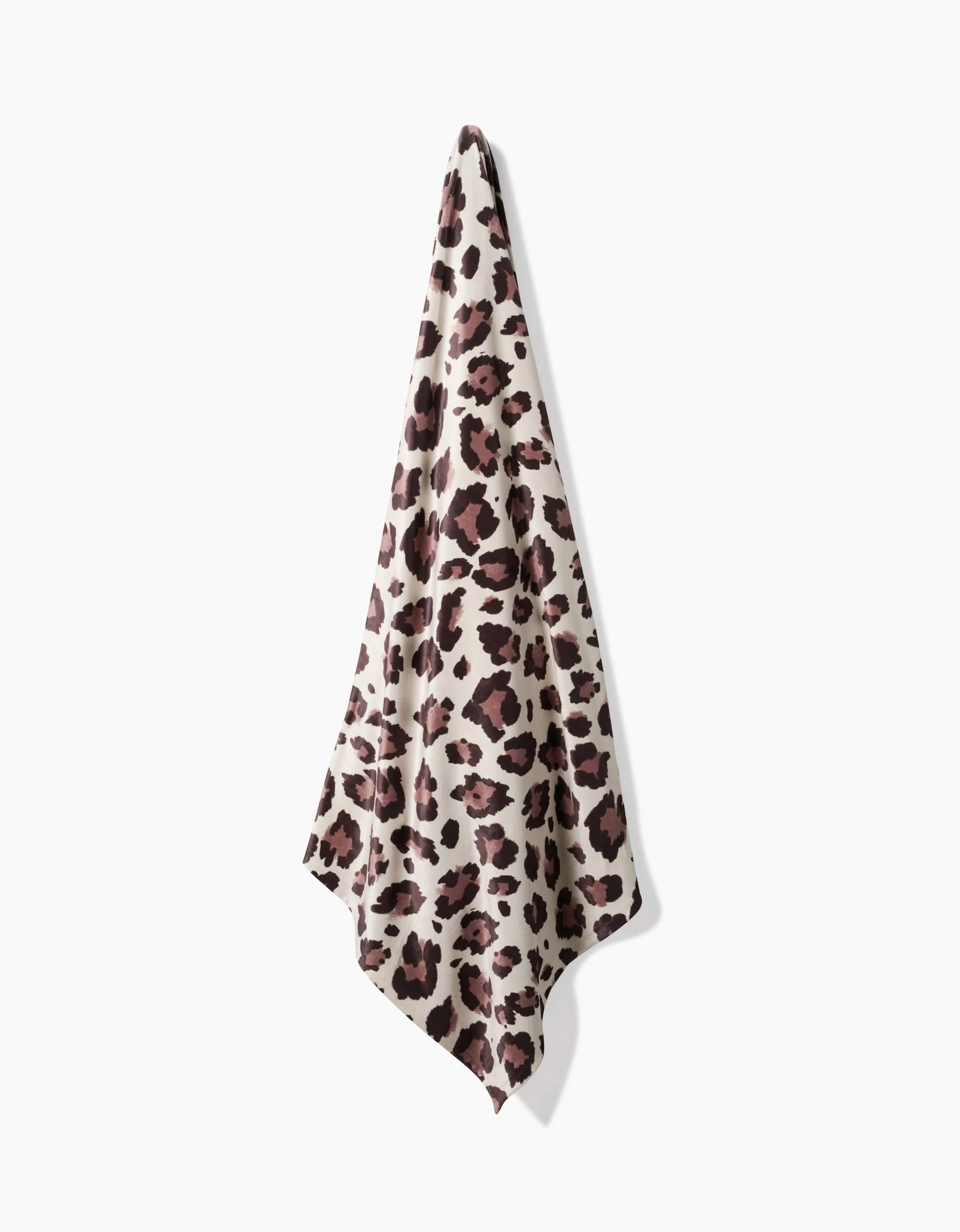 The Geometry Cheetah towel, featuring a brown, black, and beige leopard print and made from recycled materials for silky softness, hangs against a plain white background.
