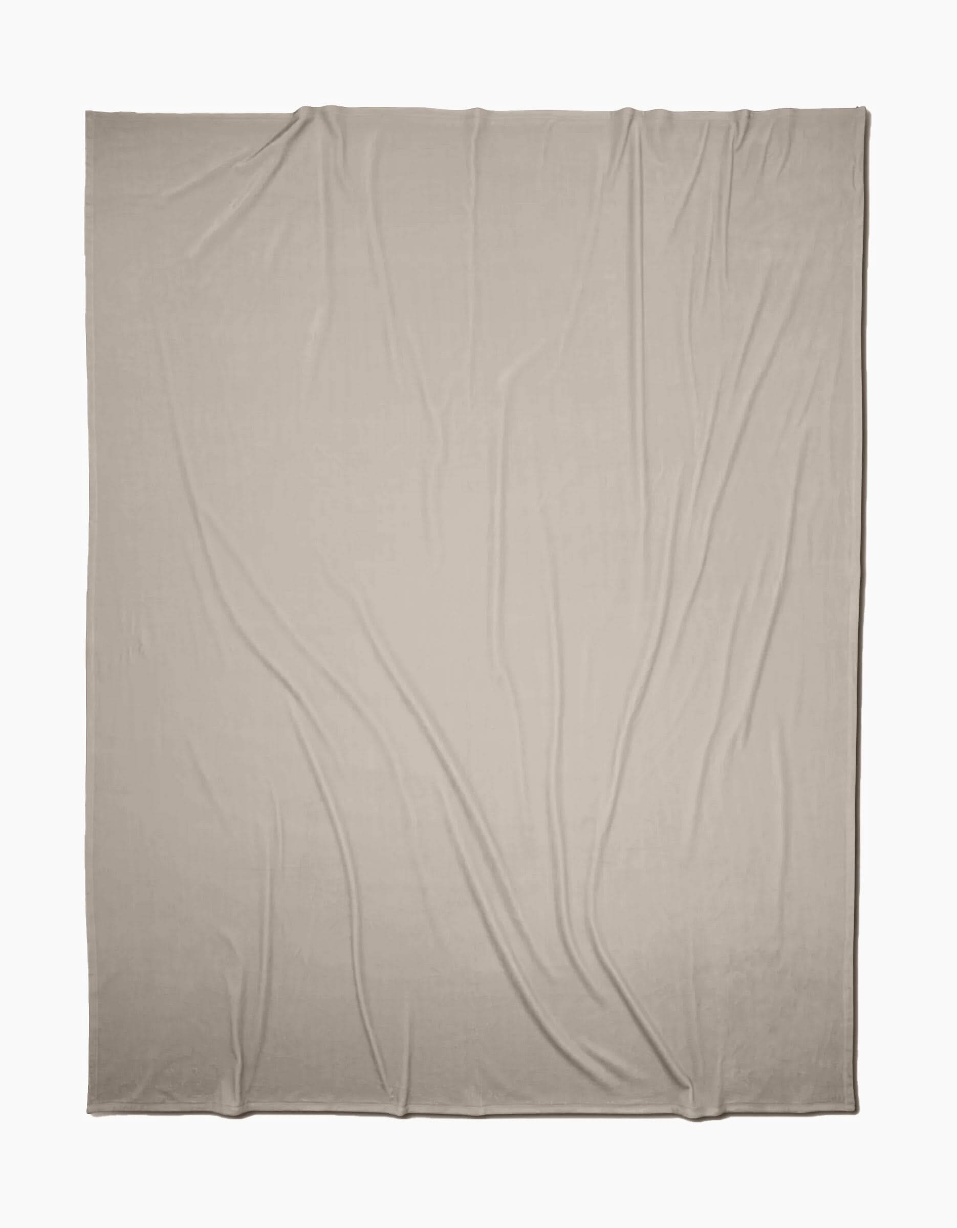 A GEOMETRY Desert Haze Butter Blanket, in light beige, is laid out flat with soft folds and wrinkles on a white background, highlighting its silky texture.