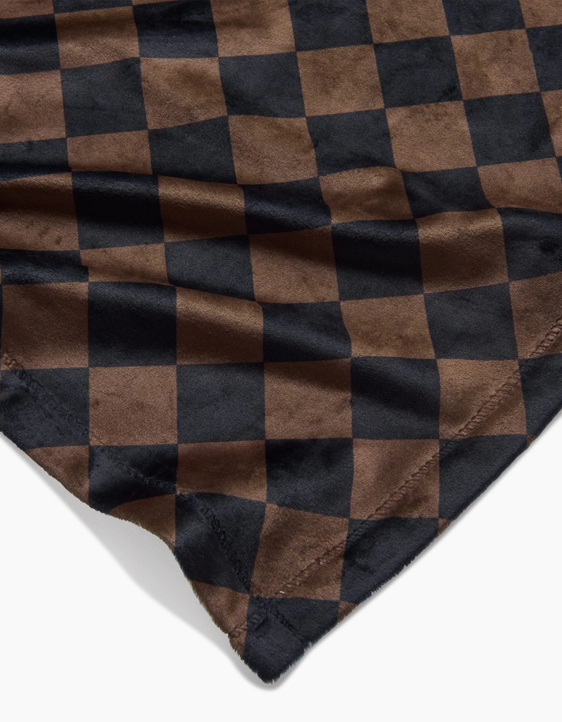 A close-up of Geometry’s Gridlock blanket reveals stitched edges and black-brown checkered fabric with wrinkles—crafted to blend style and sustainability in an eco-friendly design.