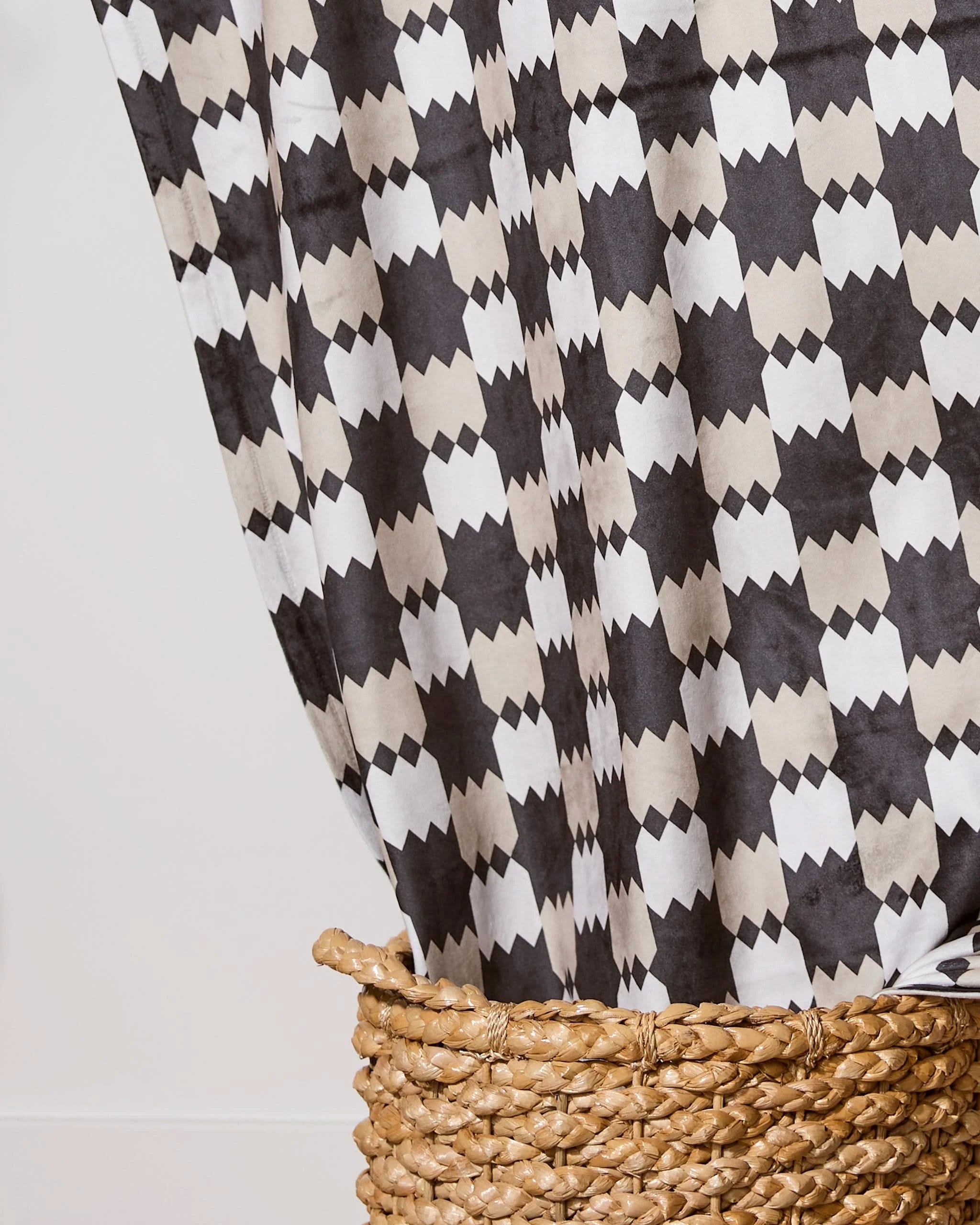 The Highland Lullaby by Geometry is a soft throw blanket with a black, white, and beige geometric pattern, draped over a woven basket to highlight its bold design.