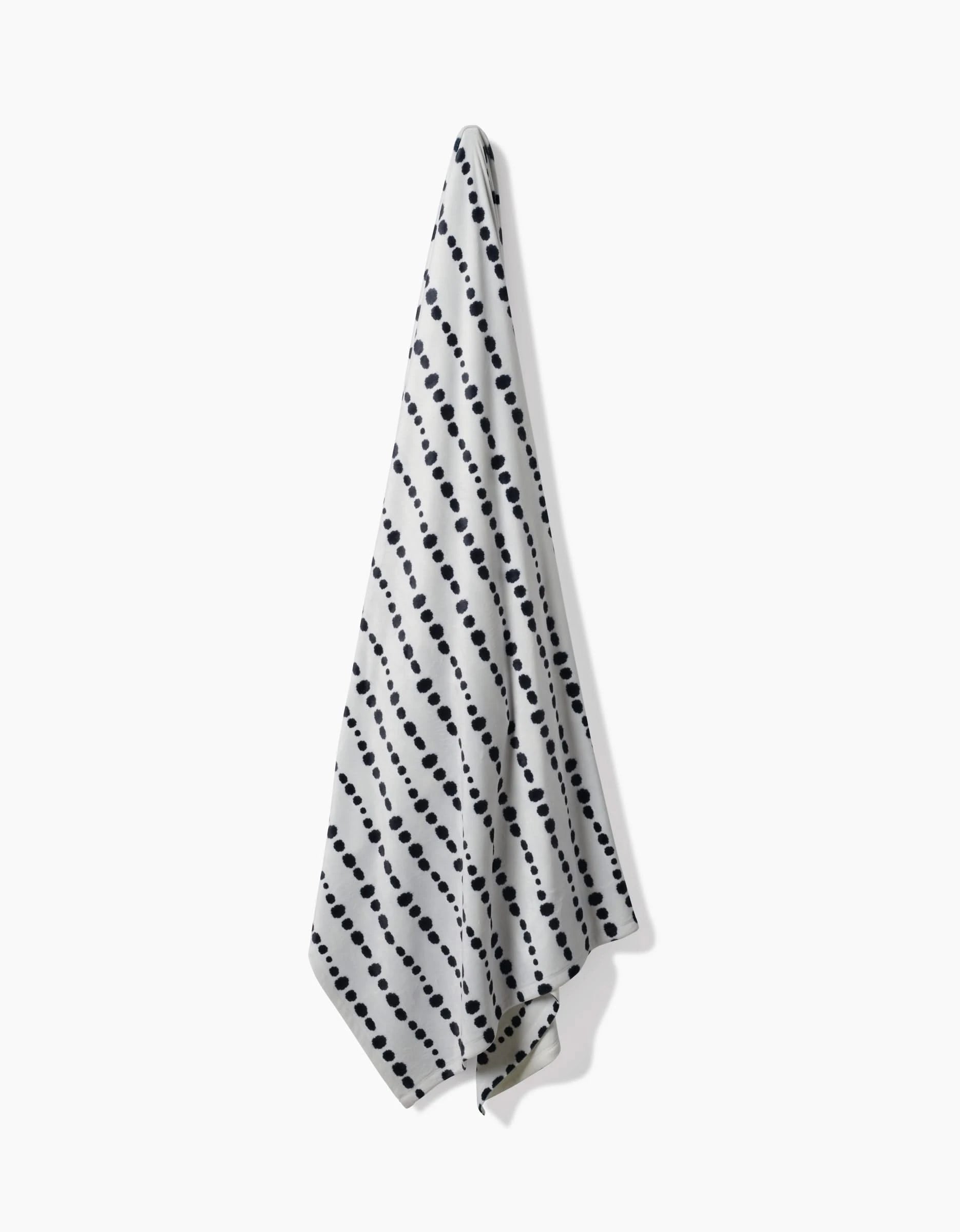 The Geometry Ink Dots towel, crafted from recycled materials and inspired by eco-friendly blankets like the Butter Blanket, features diagonal rows of black dots on white and is shown against a plain white background.