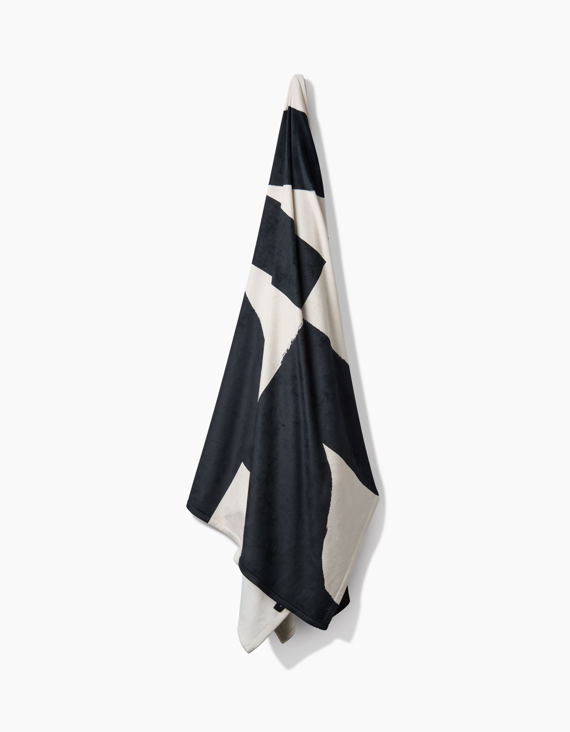 The Geometry Lined Square towel, featuring bold black and white geometric patterns and made from post-consumer recycled materials, hangs against a plain white background.