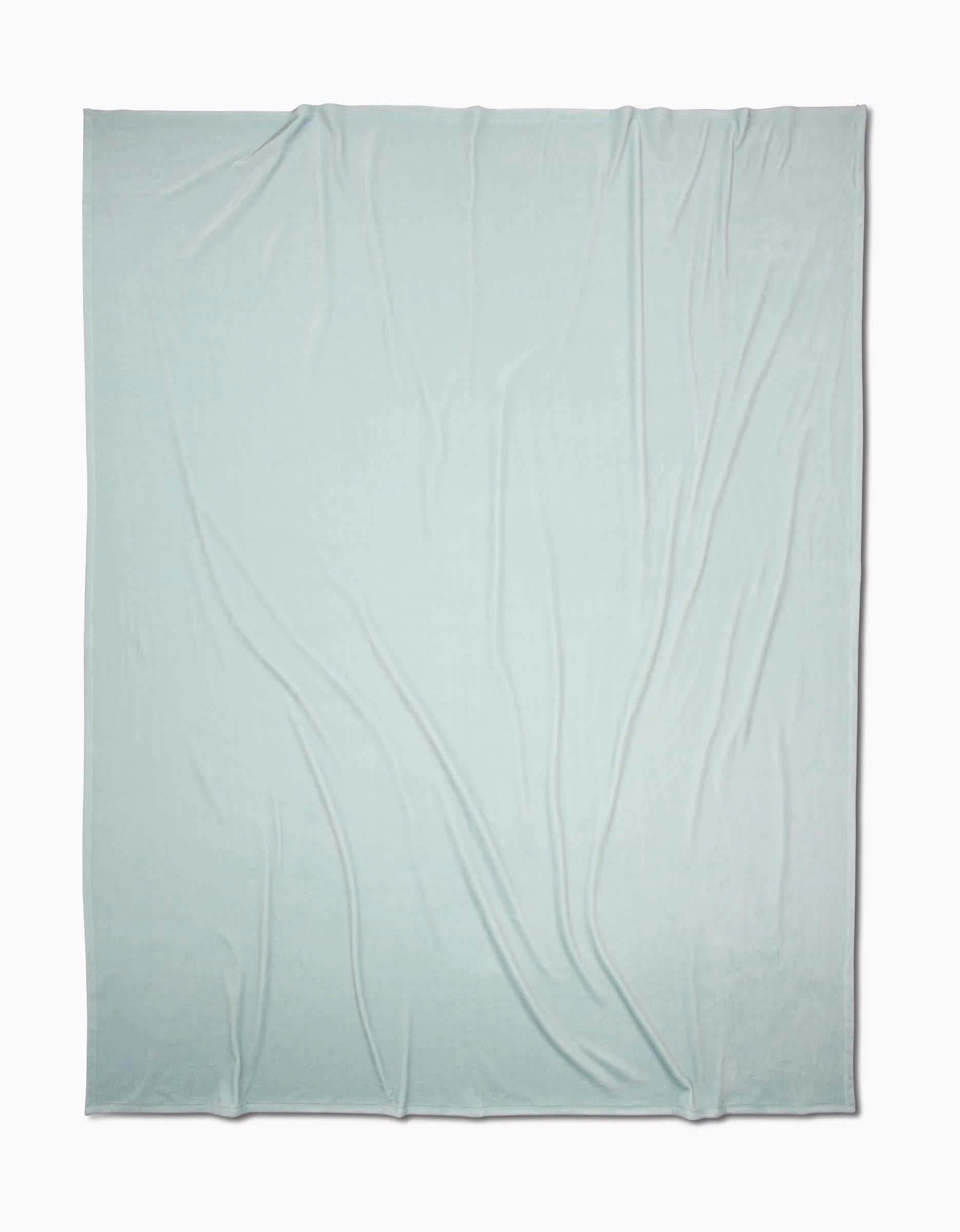 A large, Mint Drift Butter Blanket from GEOMETRY with silky softness and subtle wrinkles is spread out flat on a white background.