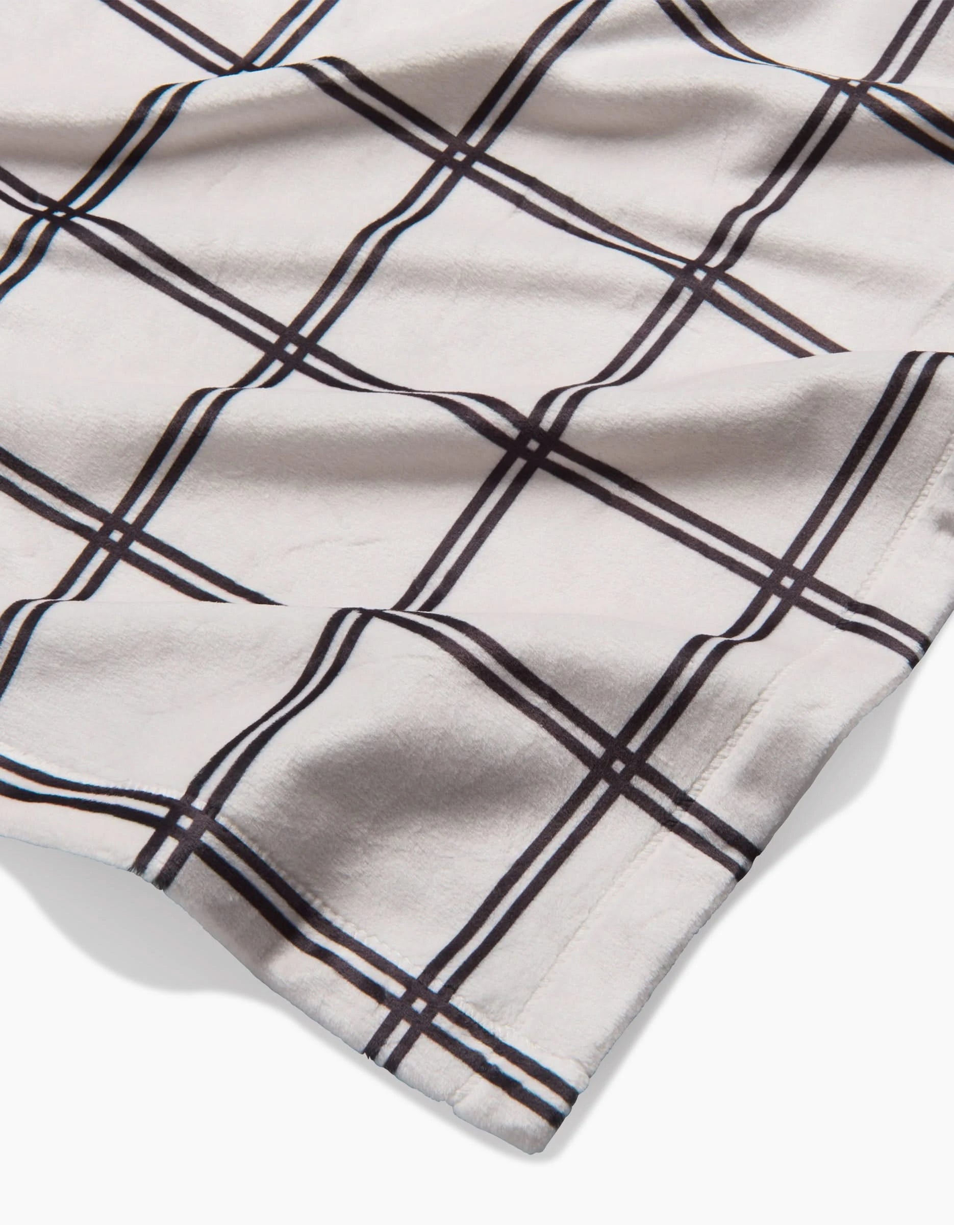 A close-up of Geometry’s Moon fabric, a soft white material with a black and brown windowpane plaid pattern, made from recycled materials and gently wrinkled on a flat surface.