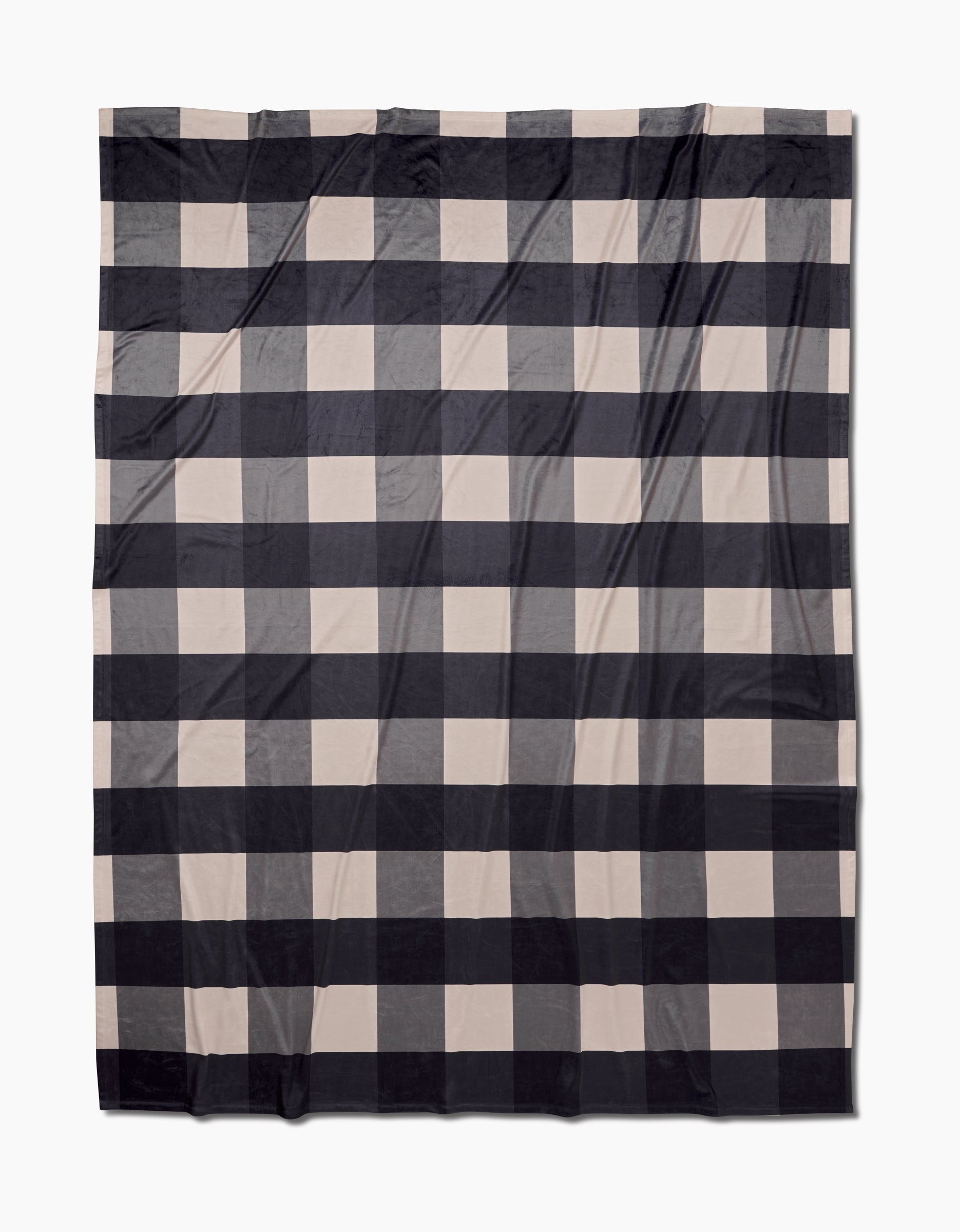 The Geometry Snowy Gingham Butter Blanket showcases a large black and beige buffalo check plaid with crisp stripes forming a grid. Slightly wrinkled, it delivers silky softness and cozy comfort.