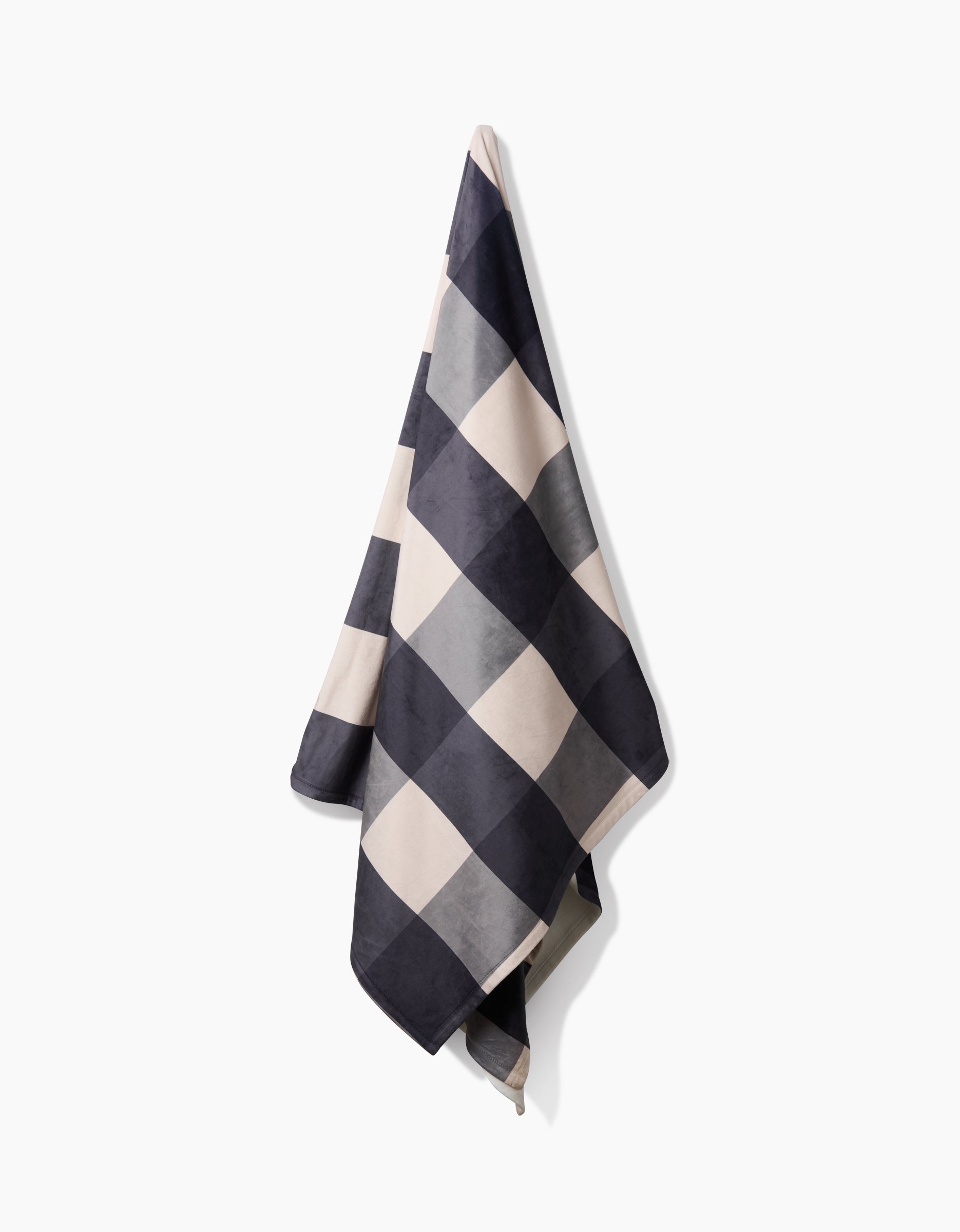 The Geometry Snowy Gingham towel, featuring a large black-and-white checkered pattern and made from recycled materials, hangs on a white wall.