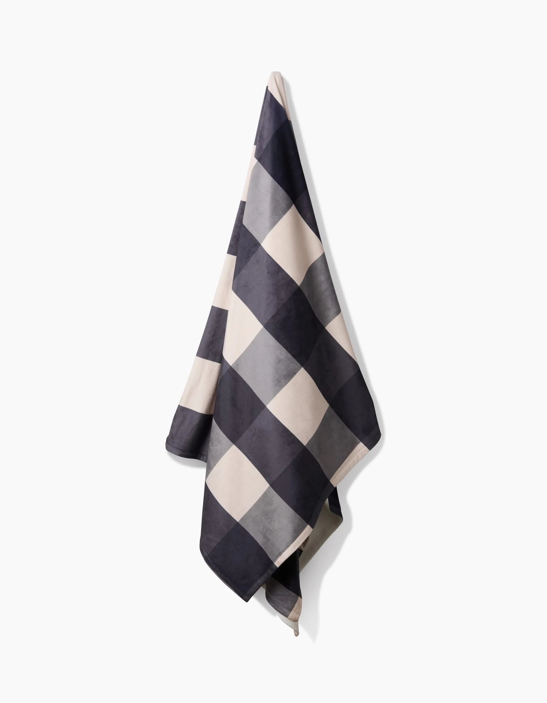 The Geometry Snowy Gingham towel, featuring a large black-and-white checkered pattern and made from recycled materials, hangs on a white wall.