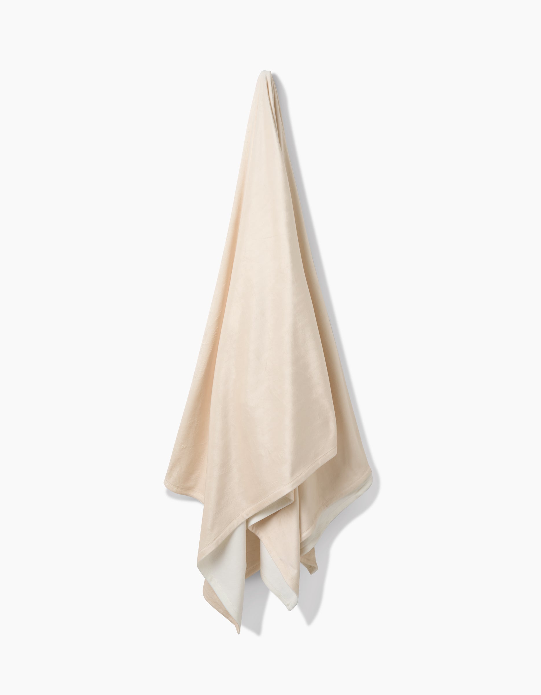 The GEOMETRY Soft Glow towel, crafted from eco-friendly recycled materials, hangs on a hook against a white background with its beige ends draping naturally.