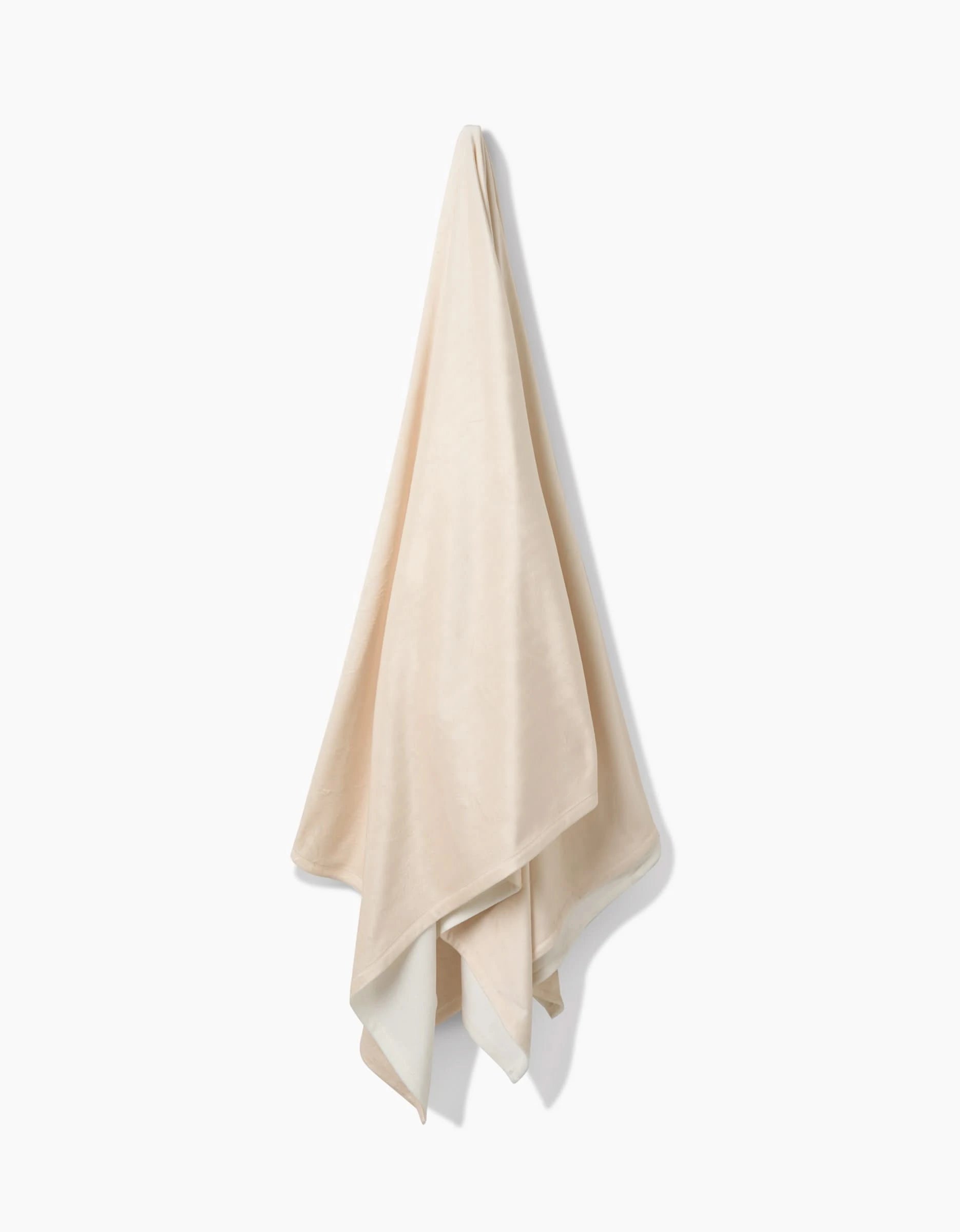 The GEOMETRY Soft Glow towel, crafted from eco-friendly recycled materials, hangs on a hook against a white background with its beige ends draping naturally.