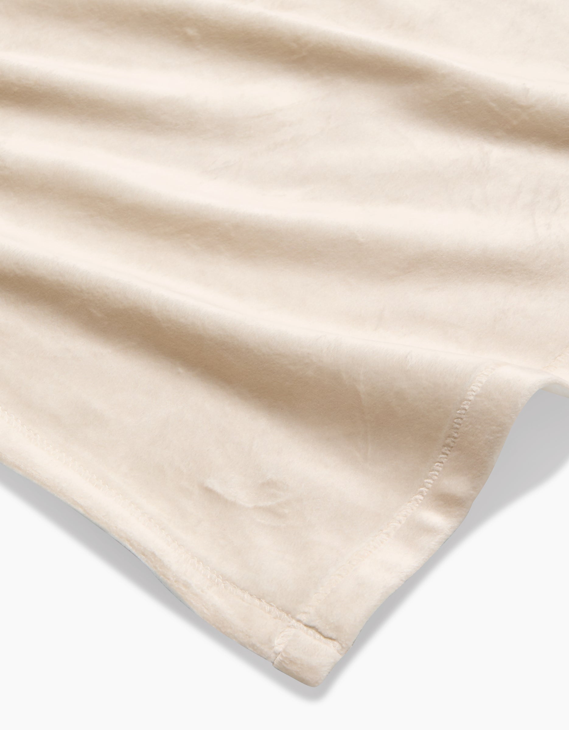 A close-up of GEOMETRY’s Soft Glow blanket, crafted from recycled materials in a soft beige shade, features a stitched hem and highlights its smooth texture and gentle folds.