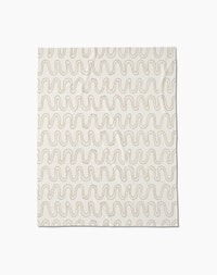 The Abstract Squiggles throw blanket by Geometry is crafted from recycled blankets for comfort and sustainability, featuring a soft cream color with evenly spaced wavy beige lines in a repeating pattern, displayed flat against a white background.