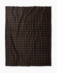 The Geometry Gridlock blanket is made from recycled materials and features a dark brown and black checkerboard pattern of small, evenly spaced squares. Subtle wrinkles add texture, and its shown against a white background.