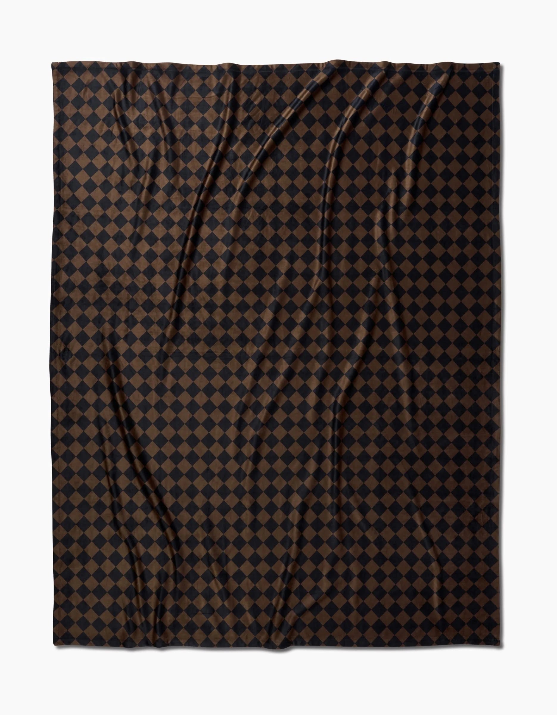 The Geometry Gridlock blanket is made from recycled materials and features a dark brown and black checkerboard pattern of small, evenly spaced squares. Subtle wrinkles add texture, and its shown against a white background.