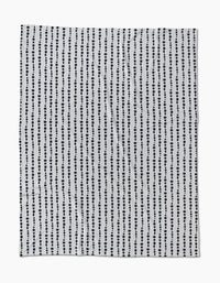 The Geometry Ink Dots Butter Blanket features vertical rows of evenly spaced black dots on white, offering a simple, modern polka dot design—crafted from recycled materials for an eco-friendly touch.
