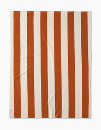The Radiance Butter Blanket by Geometry features wide vertical stripes in alternating orange and white, crafted from recycled materials and displayed flat on a white background.
