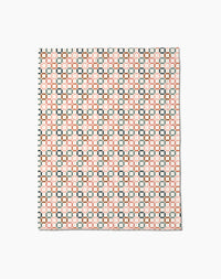 The Russet Crossroads Butter Blanket by Charlie Rowan Designs features a geometric grid of black, red, and cream squares on white, crafted from recycled materials for an eco-friendly touch.