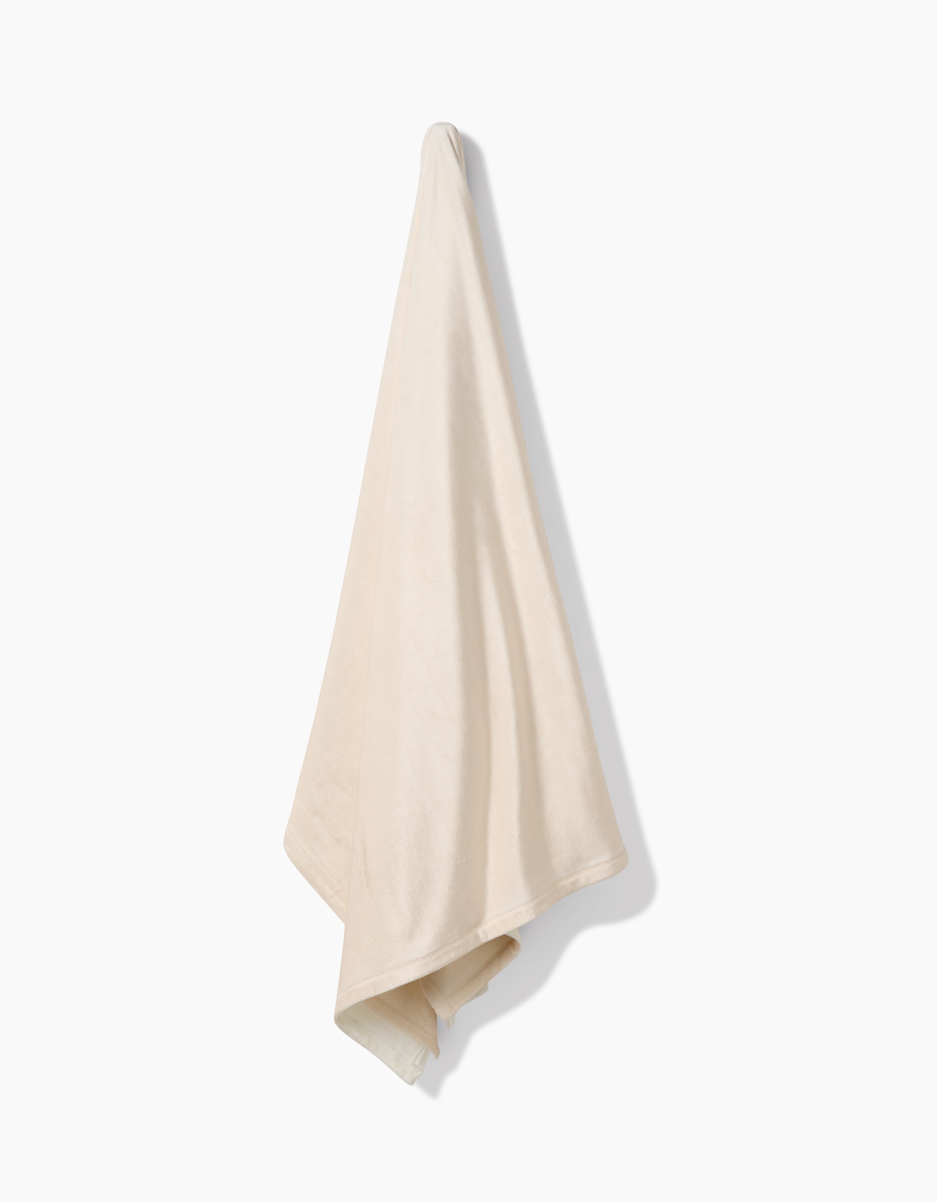 A Soft Glow towel by GEOMETRY, crafted from eco-friendly recycled materials, hangs from a single point against a plain white background, casting a soft shadow on the wall.