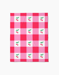 The Geometry Sweet Cherry Gingham throw blanket features a pink and red checkered pattern with white squares, each adorned with two red cherries and green leaves—adding cozy, cheerful comfort to any space.