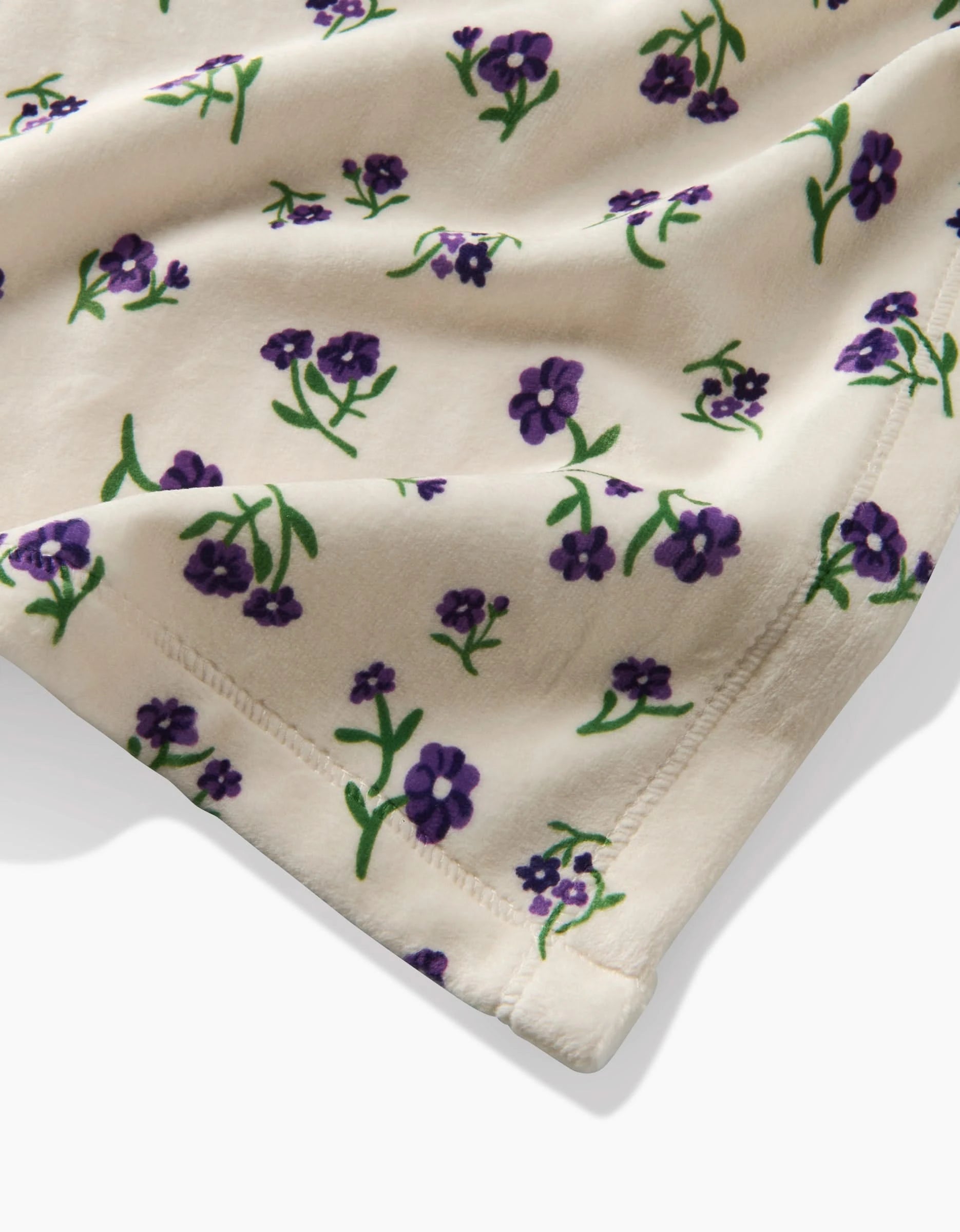 The Violet Sound by Geometry is a cream-colored Butter Blanket made from recycled materials, featuring purple flowers and green stems with neat stitching. Its soft, plush fabric is perfect for cozy, sustainable blankets or comfy clothing.
