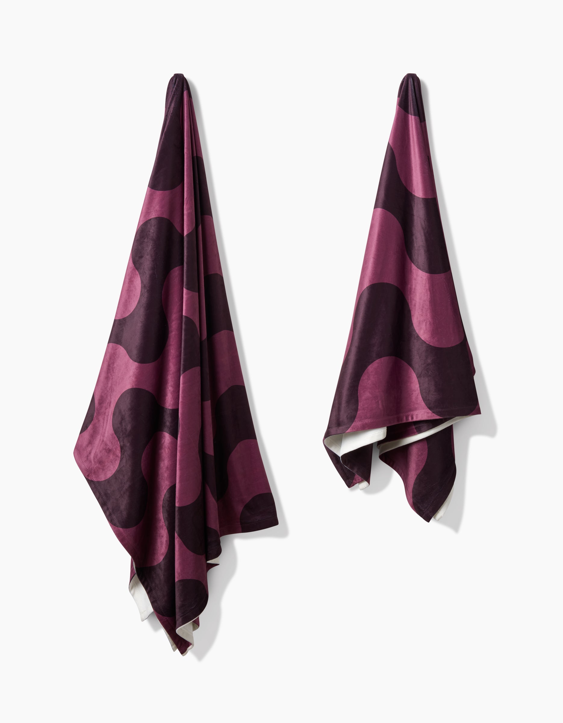 Two Groove With Me towels by Geometry, featuring a bold wavy dark purple and magenta pattern and made from recycled materials, hang separately on a white wall.