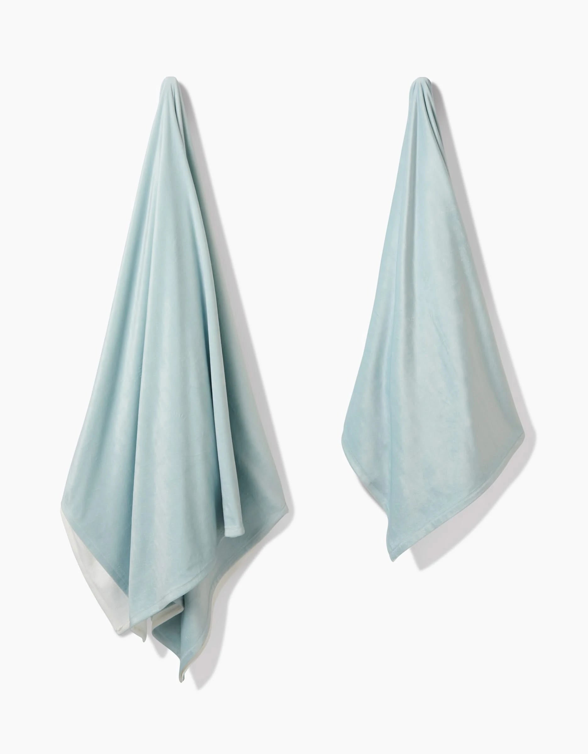Two GEOMETRY Mint Drift towels, crafted from silky post-consumer recycled materials, hang separately on hooks against a plain white background.