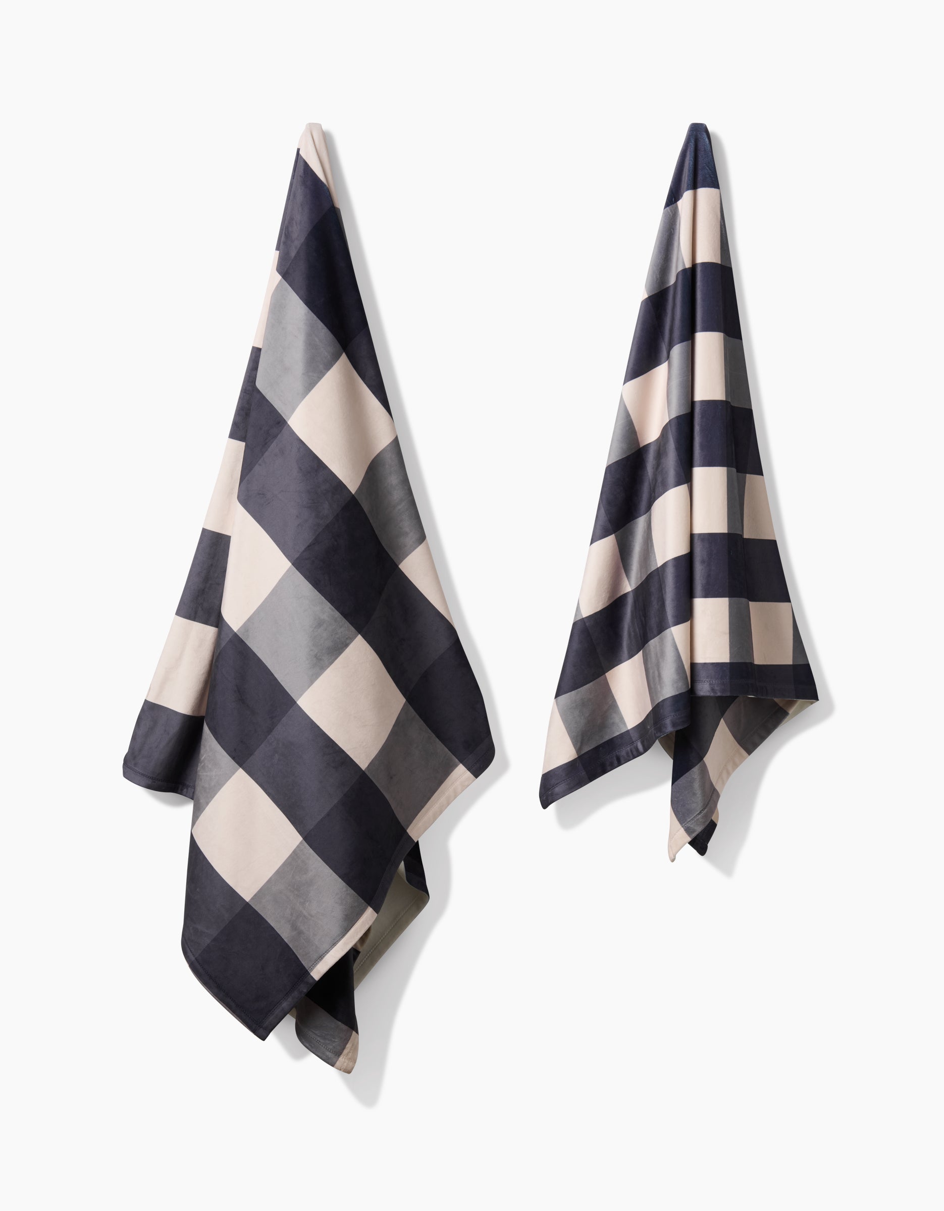 Two Snowy Gingham towels by Geometry, featuring a bold black and white checkerboard design and made from recycled materials, hang separately against a plain white background.