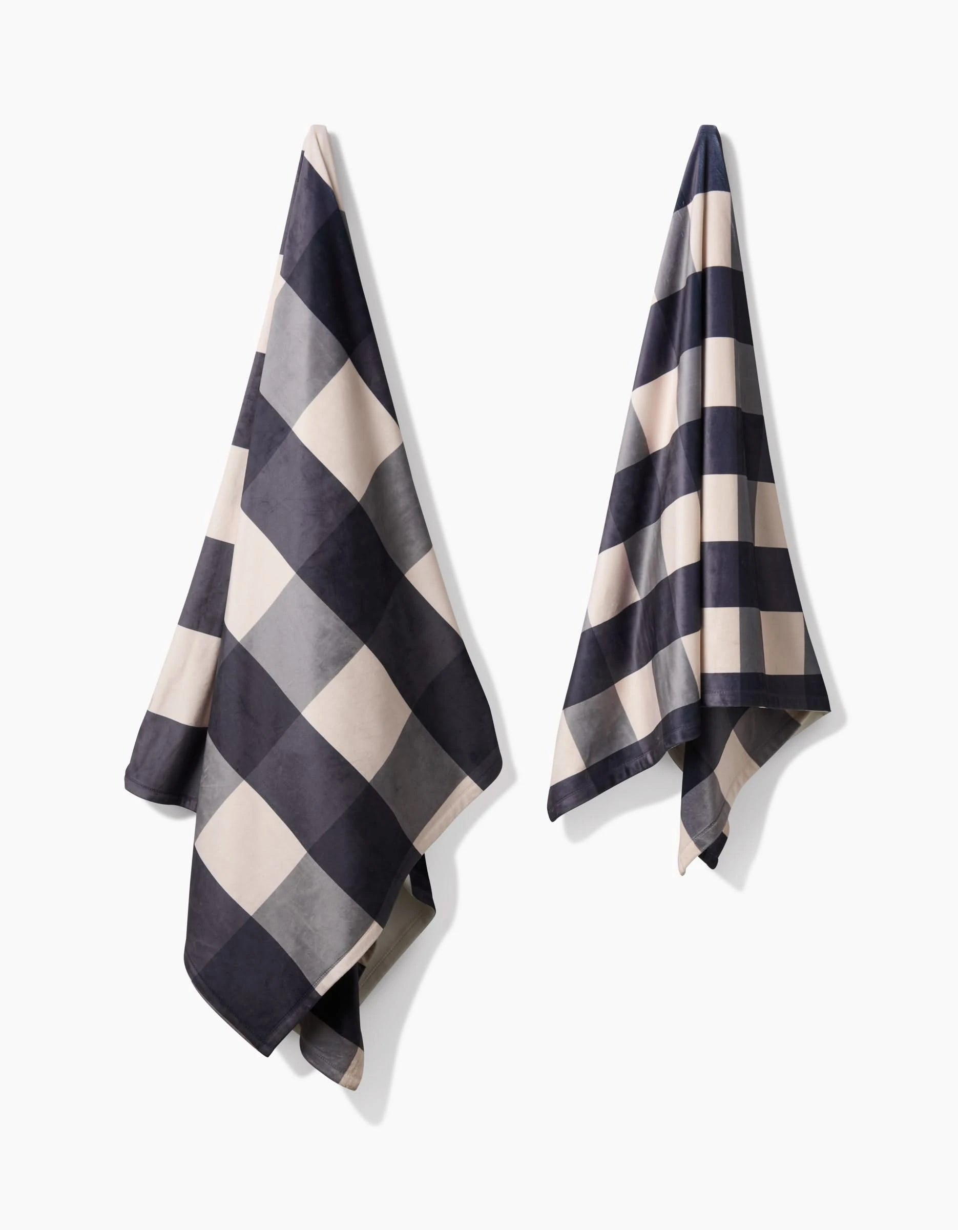 Two Snowy Gingham towels by Geometry, featuring a bold black and white checkerboard design and made from recycled materials, hang separately against a plain white background.