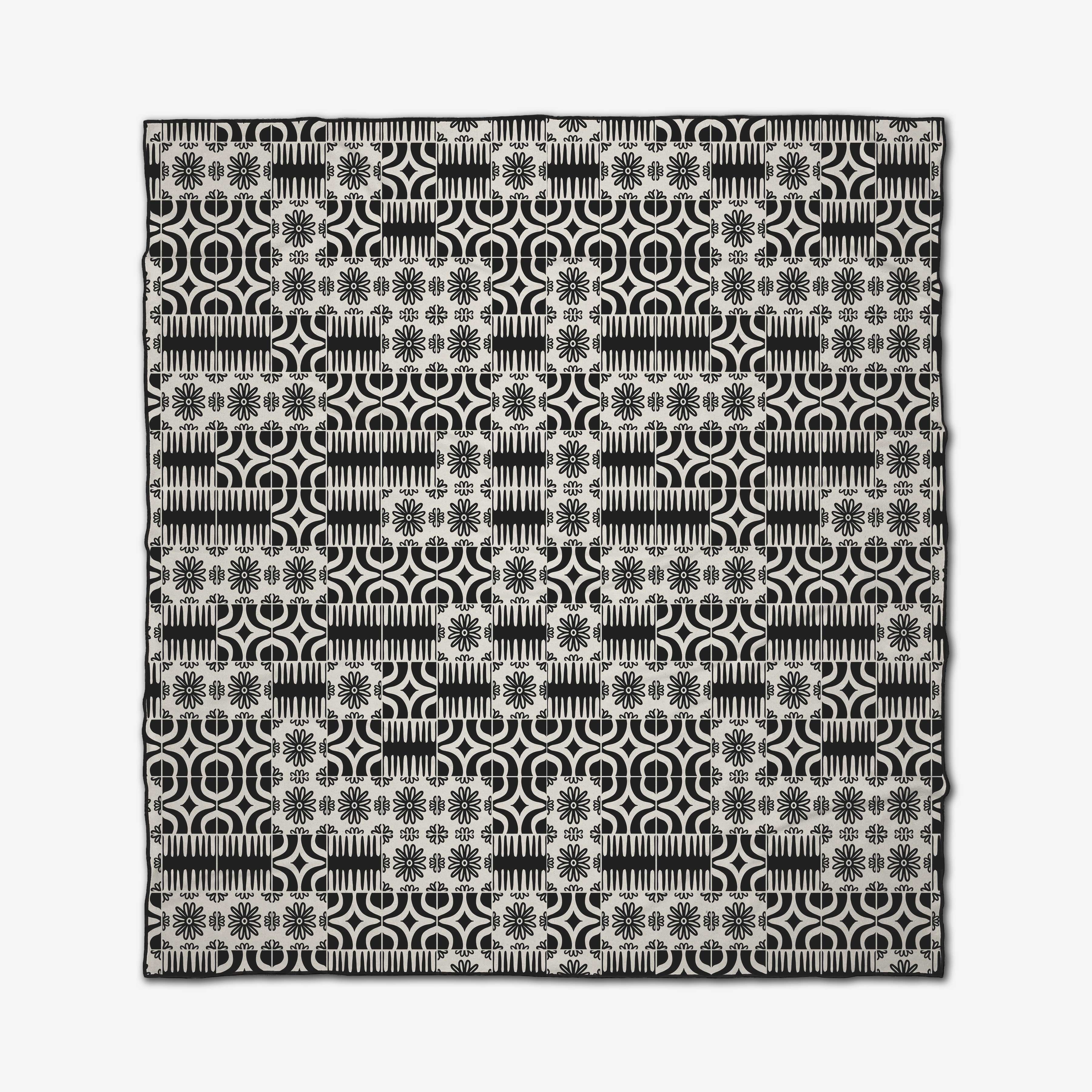 The GEOMETRY Bohemian Mosaic is a square beach blanket crafted from recycled materials, showcasing a black and white geometric design with circles, lines, and floral motifs in a grid pattern.