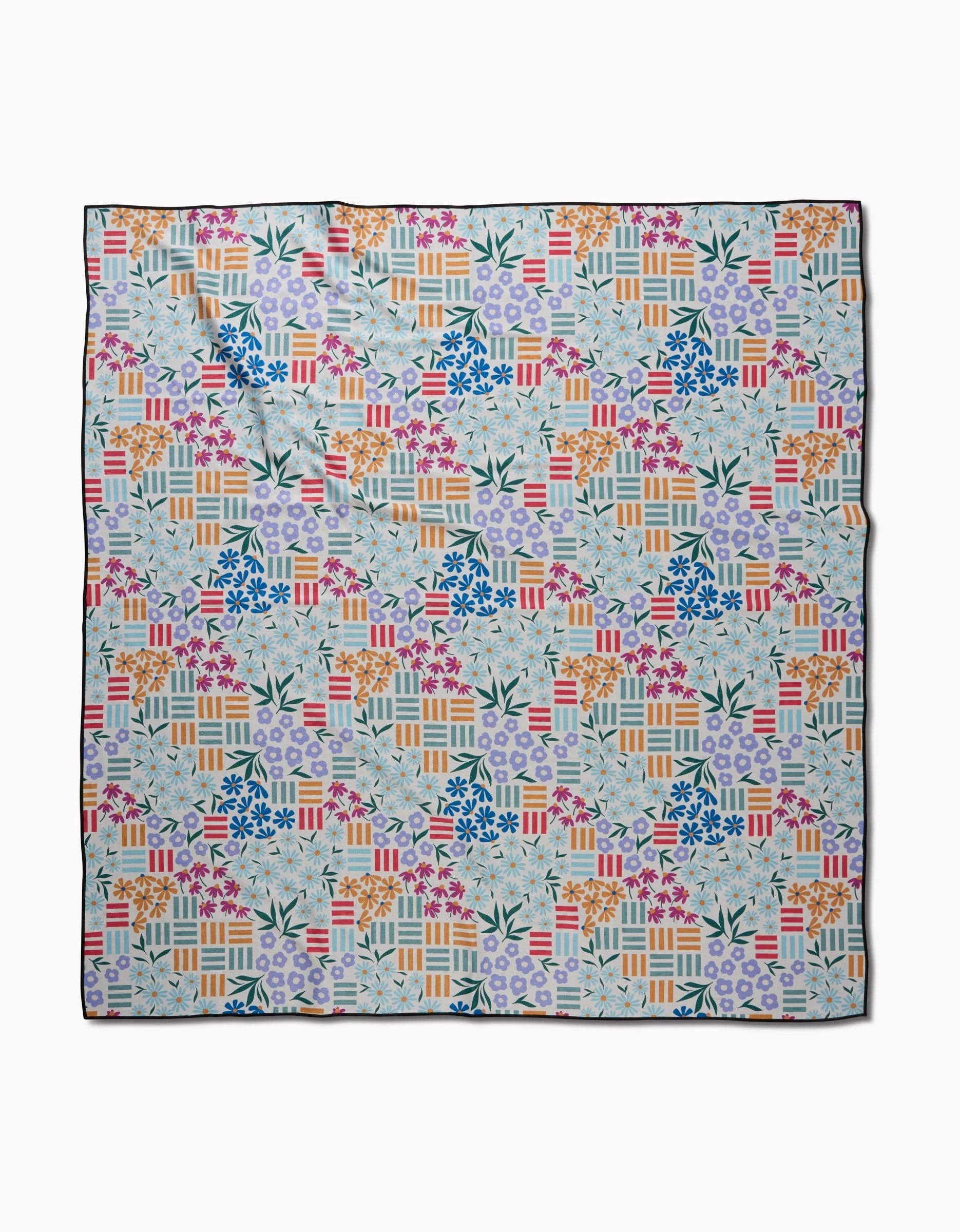 The Floral Garden Beach Blanket by Charlie Rowan Designs features a square shape with a vibrant geometric and floral patchwork in pink, orange, blue, and green on a light background, crafted from recycled materials.