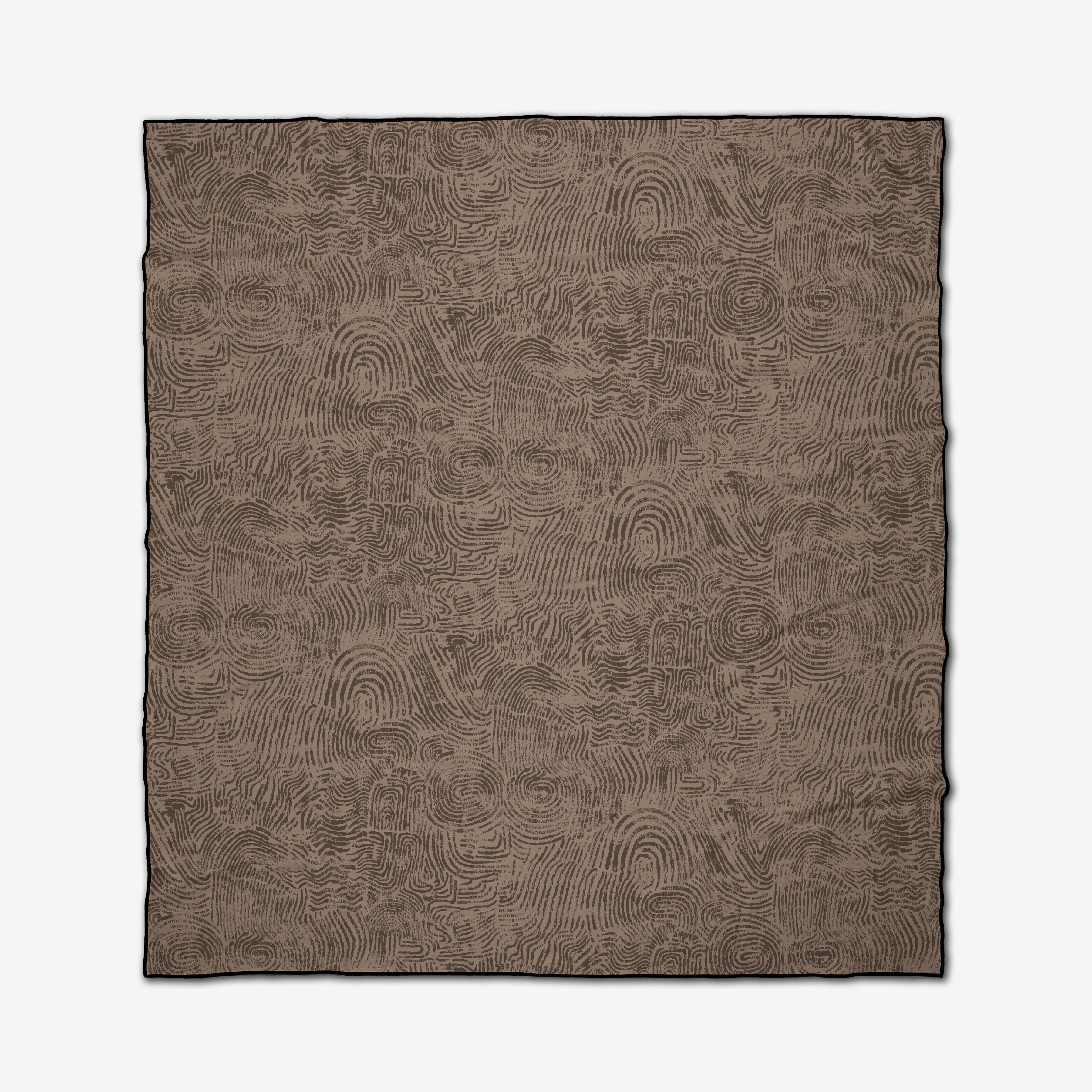 The Imprint beach blanket by Studio Jeannot is rectangular, brown, and made from recycled materials. Black edges frame its surface, which is fully covered in an abstract pattern of swirling, fingerprint-like lines.