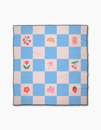 The Little Picnic Things beach blanket by Letters By Shells is a blue and white checkerboard, quick-drying, made from recycled materials, and decorated with cherries, a croissant, jar, flower, bow, strawberry, and cake.