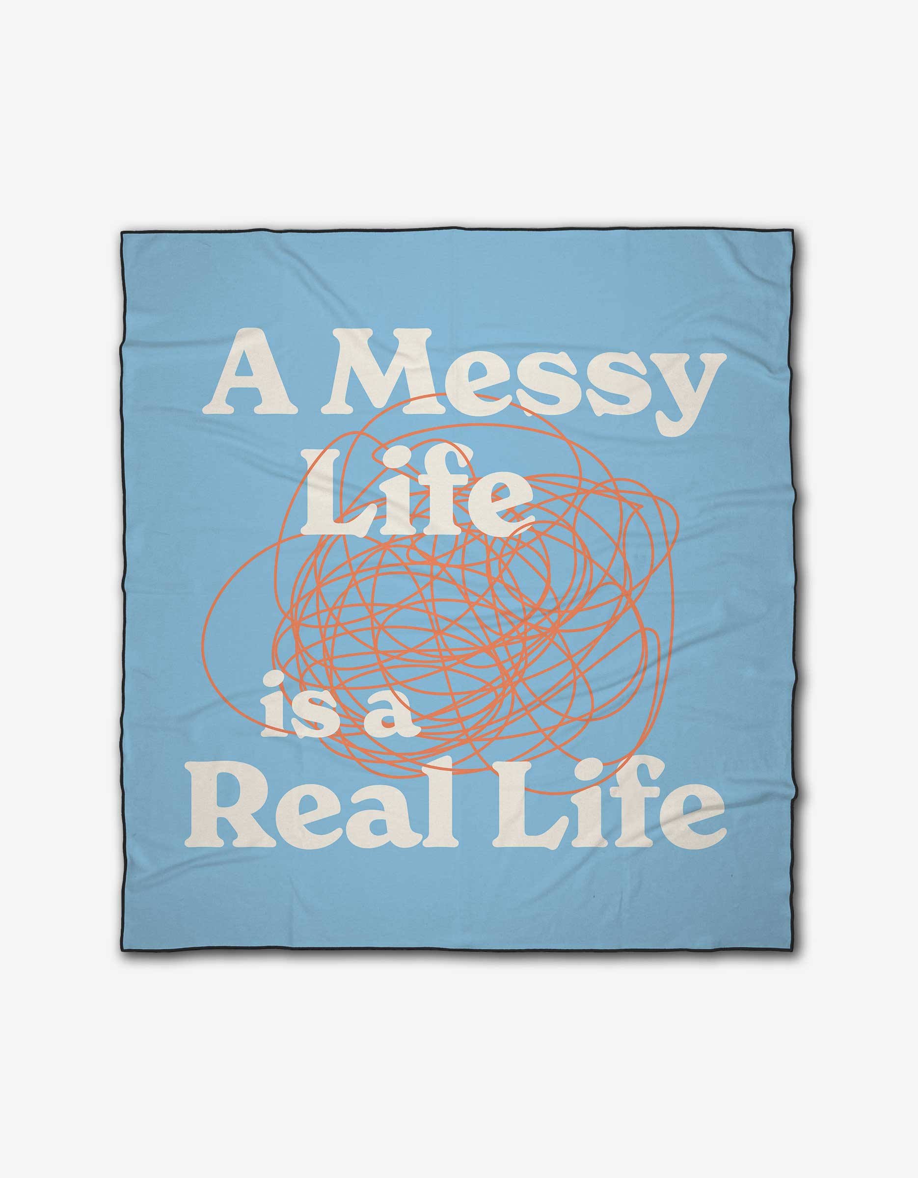 The Messy Life beach blanket by Quotes by Christie is light blue, made from recycled materials, featuring large white text “A Messy Life is a Real Life” and an orange scribble design in the center.