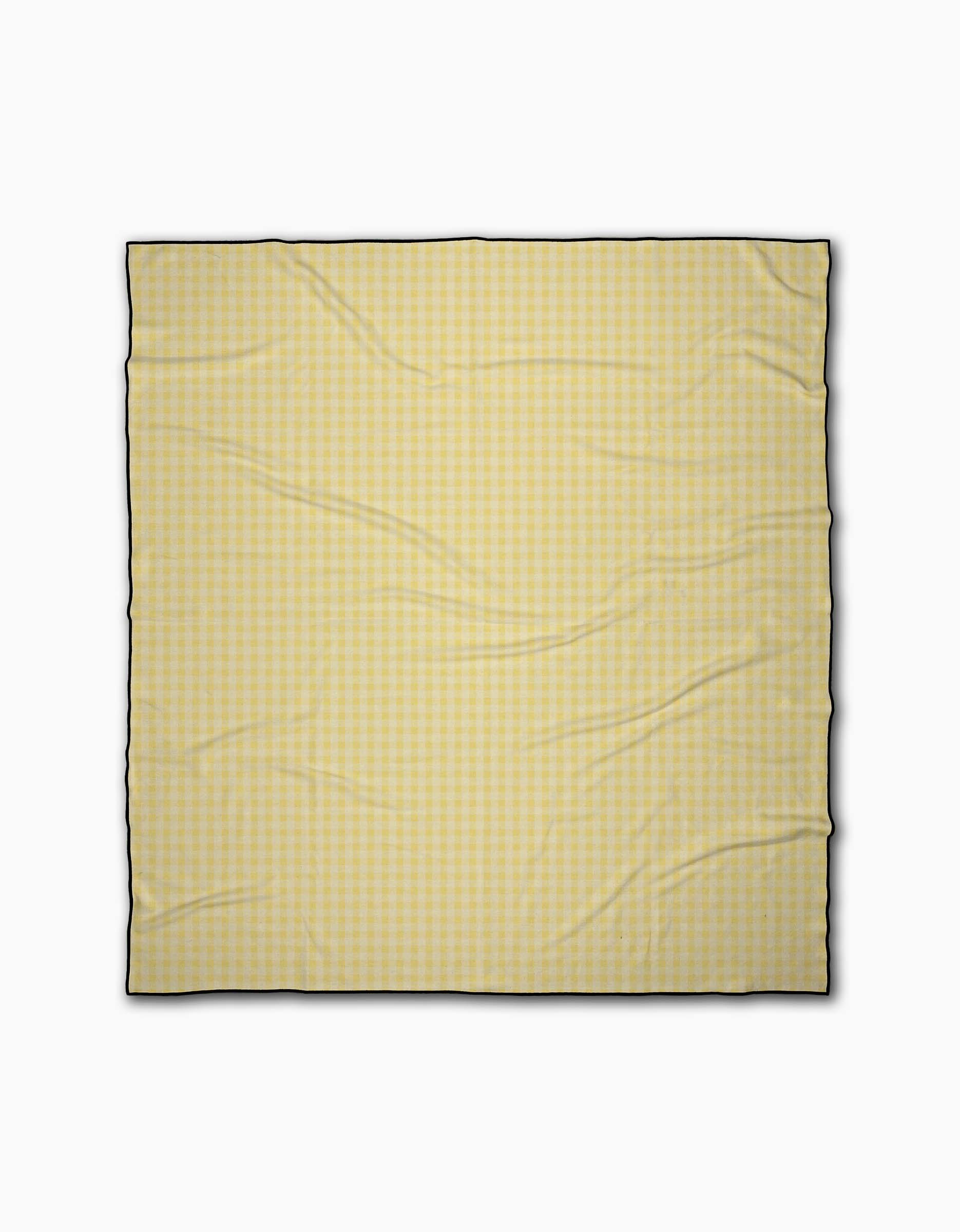 The Geometry Sunspread is a square, light yellow beach blanket with a subtle gingham check, black border, and slightly wrinkled texture. Made from quick-drying recycled materials, it’s shown on a plain white background.