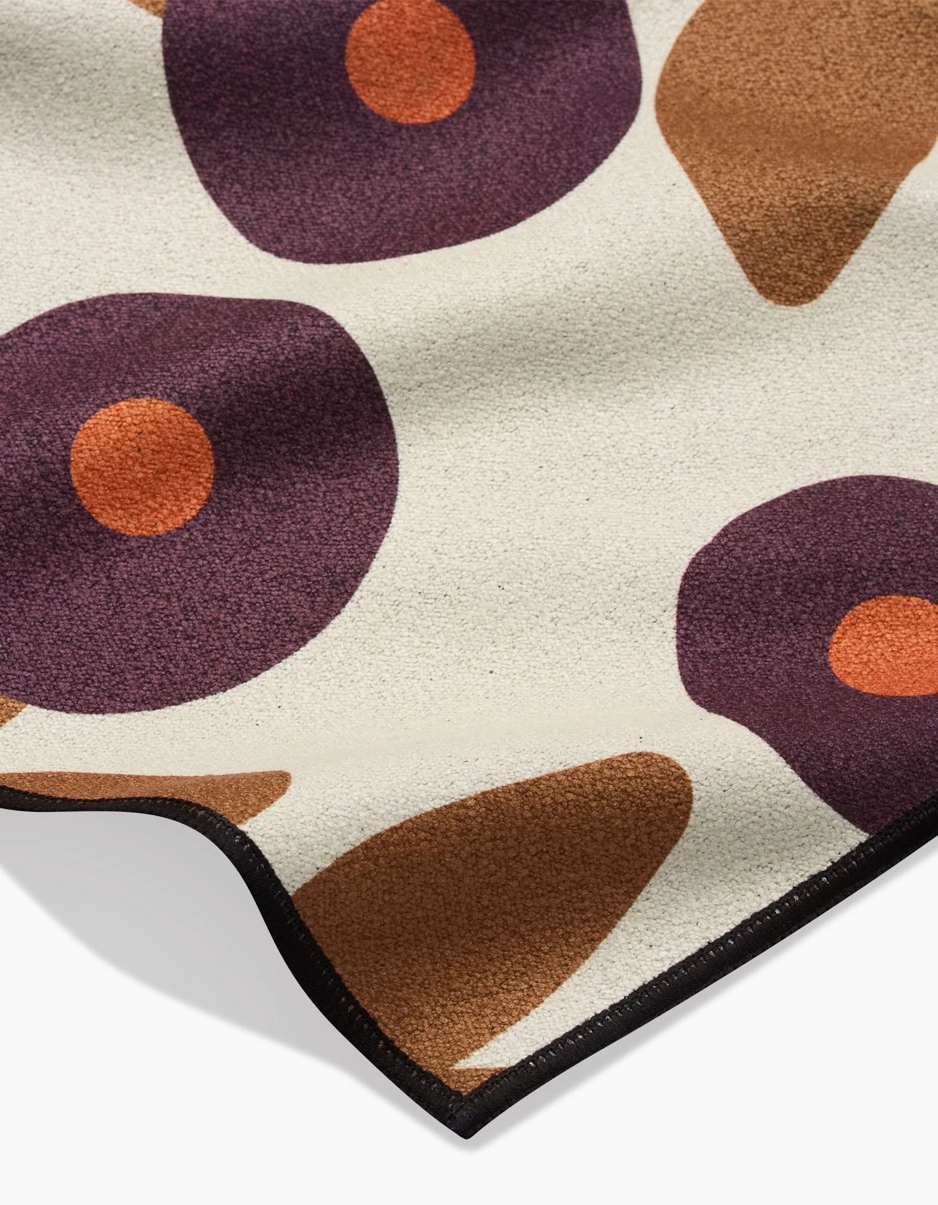 A close-up of the Swirling Vines recycled beach blanket by Lizzie Clark, featuring abstract purple circles with orange centers, brown leaf-like accents on a beige background, and finished with black trim.