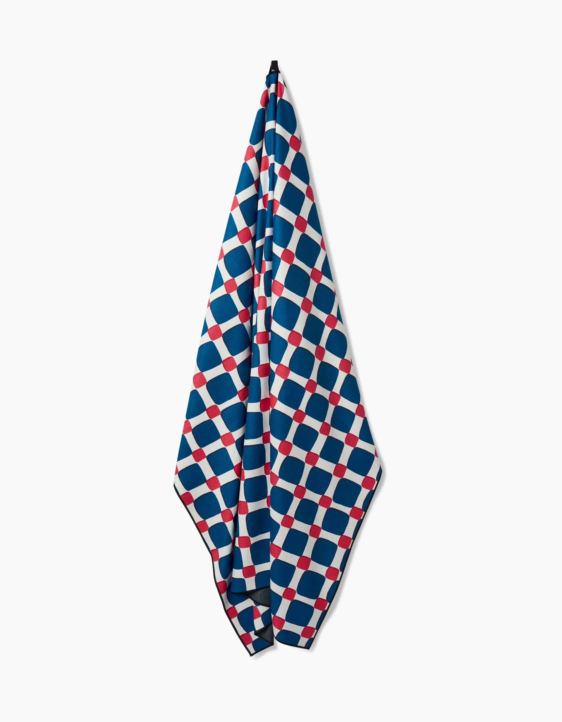 The Box Check Picnic towel by Hufton Studio hangs vertically and dries quickly, showcasing a geometric grid of blue, white, and red squares and circles on a crisp white background.