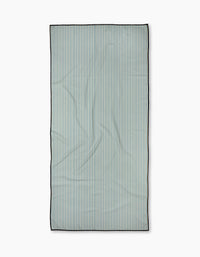 The Clean Slate beach towel by Susan Heid is rectangular and quick-drying, featuring thin, evenly spaced vertical blue and white stripes with a dark border, shown on a plain white background.
