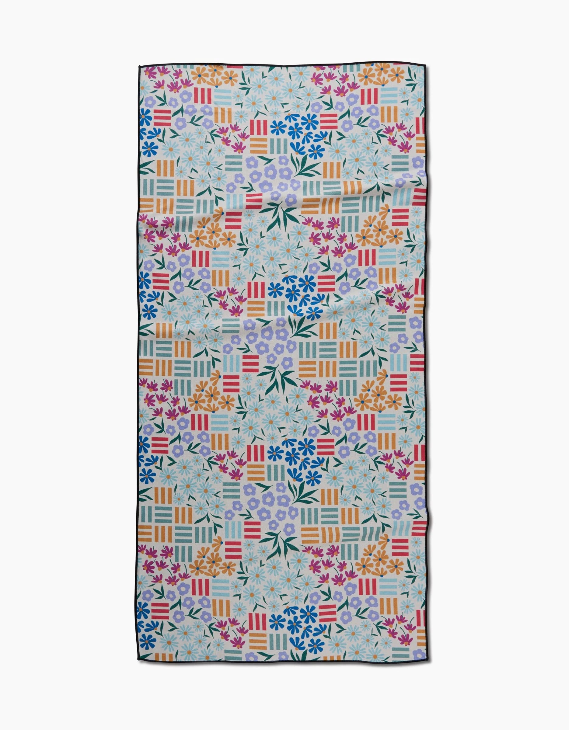 The Floral Garden beach towel by Charlie Rowan Designs is made from recycled materials and features a colorful geometric and floral pattern in blue, pink, orange, and green. Quick-drying—perfect for your next trip to the shore.