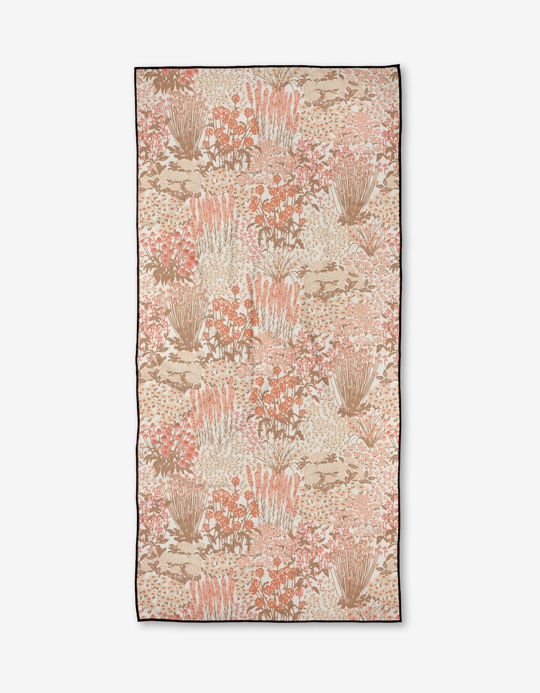 The Hufton Studio Garden Bloom towel is a rectangular beach towel with clusters of peach, pink, beige, and brown florals on quick-drying recycled fabric, finished with a dark thin border.