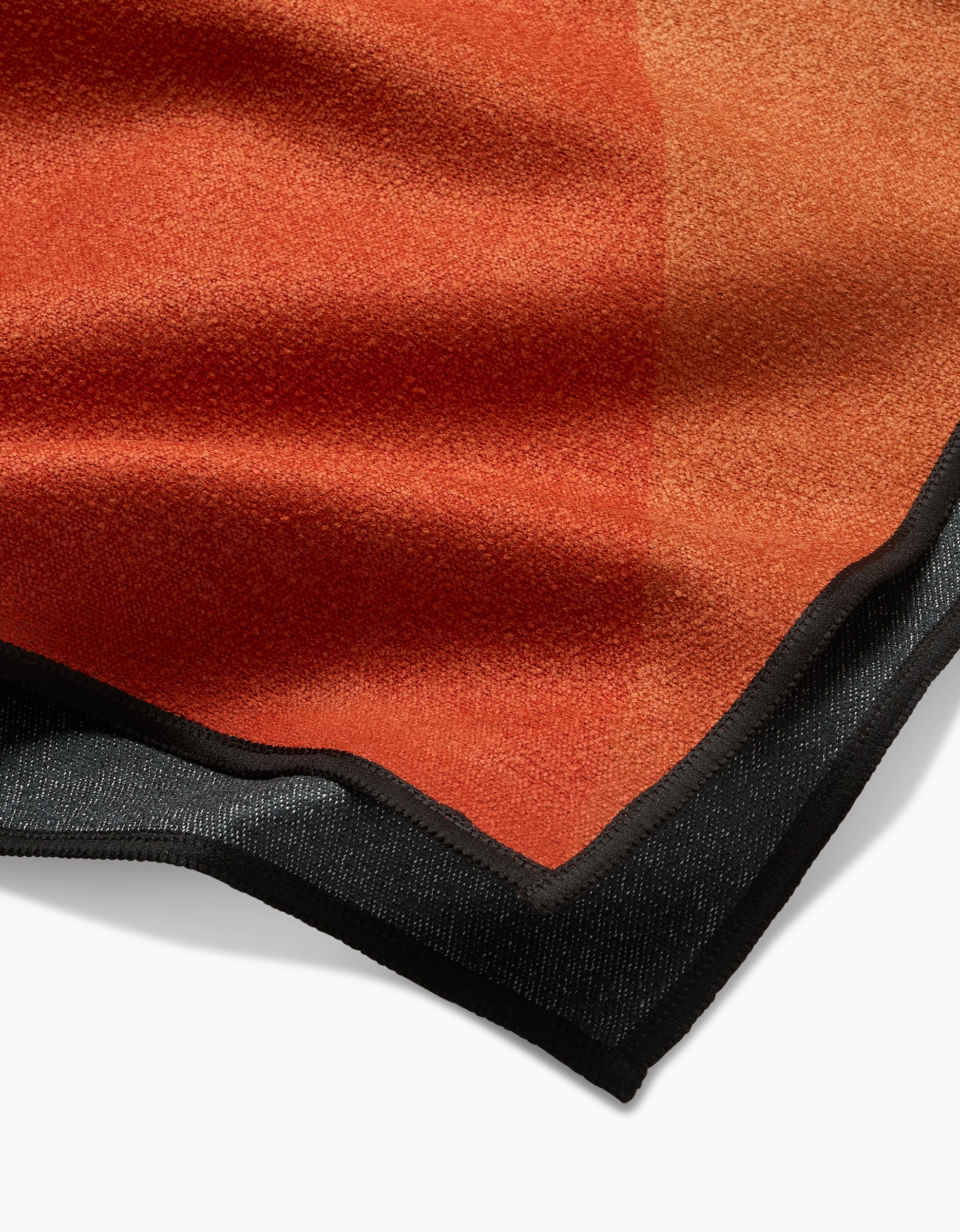 A close-up of the Megan Roy In The Desert Geometry Micro-loop Beach Towel, featuring a soft, textured orange surface with a dark border, crafted from post-consumer recycled materials and set against a white background.