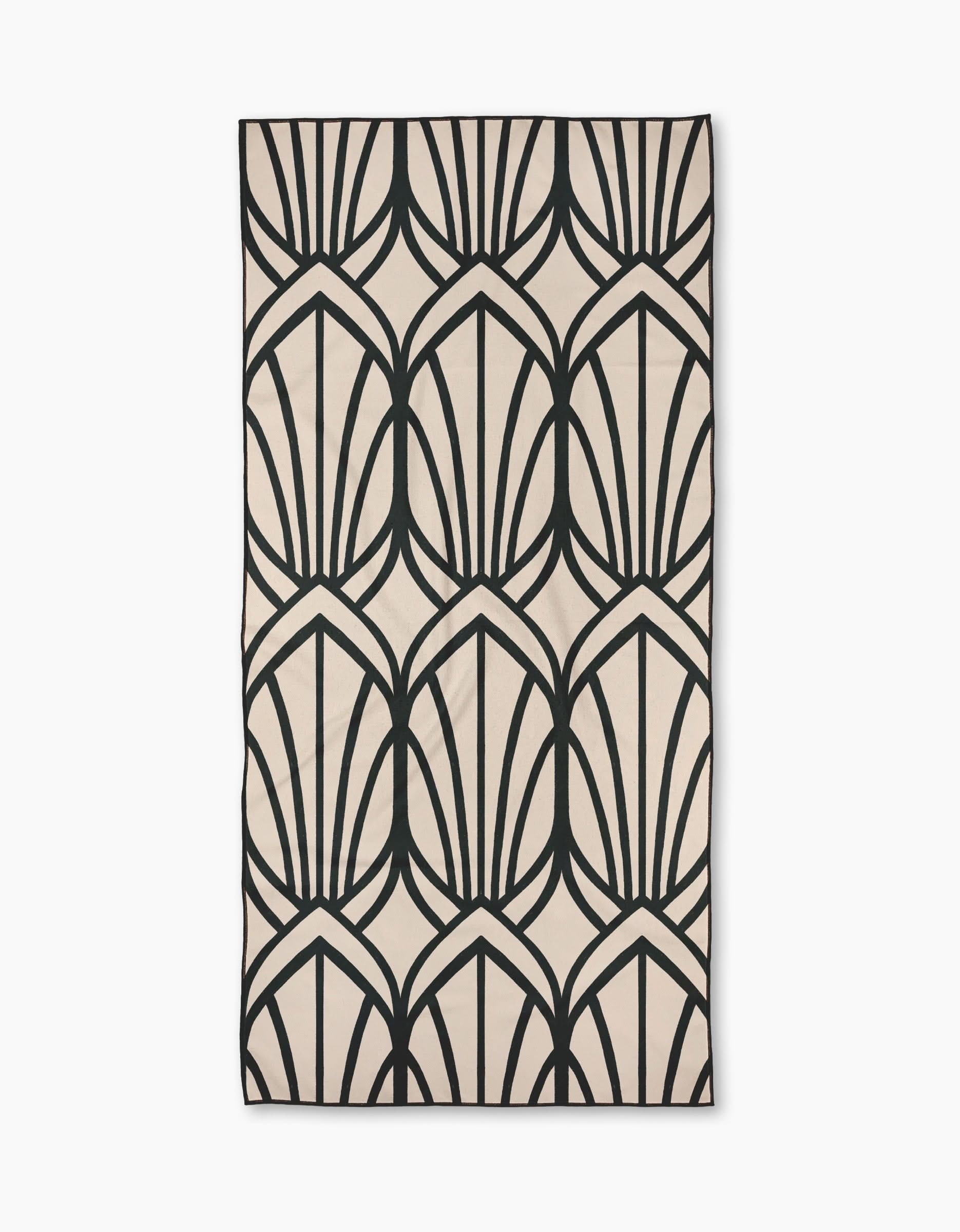 The Jocelyn rug by Amy MacCready features a beige background with a bold, repeating black geometric pattern of overlapping leaves or fans. Symmetrical and modern, it’s crafted from recycled materials.