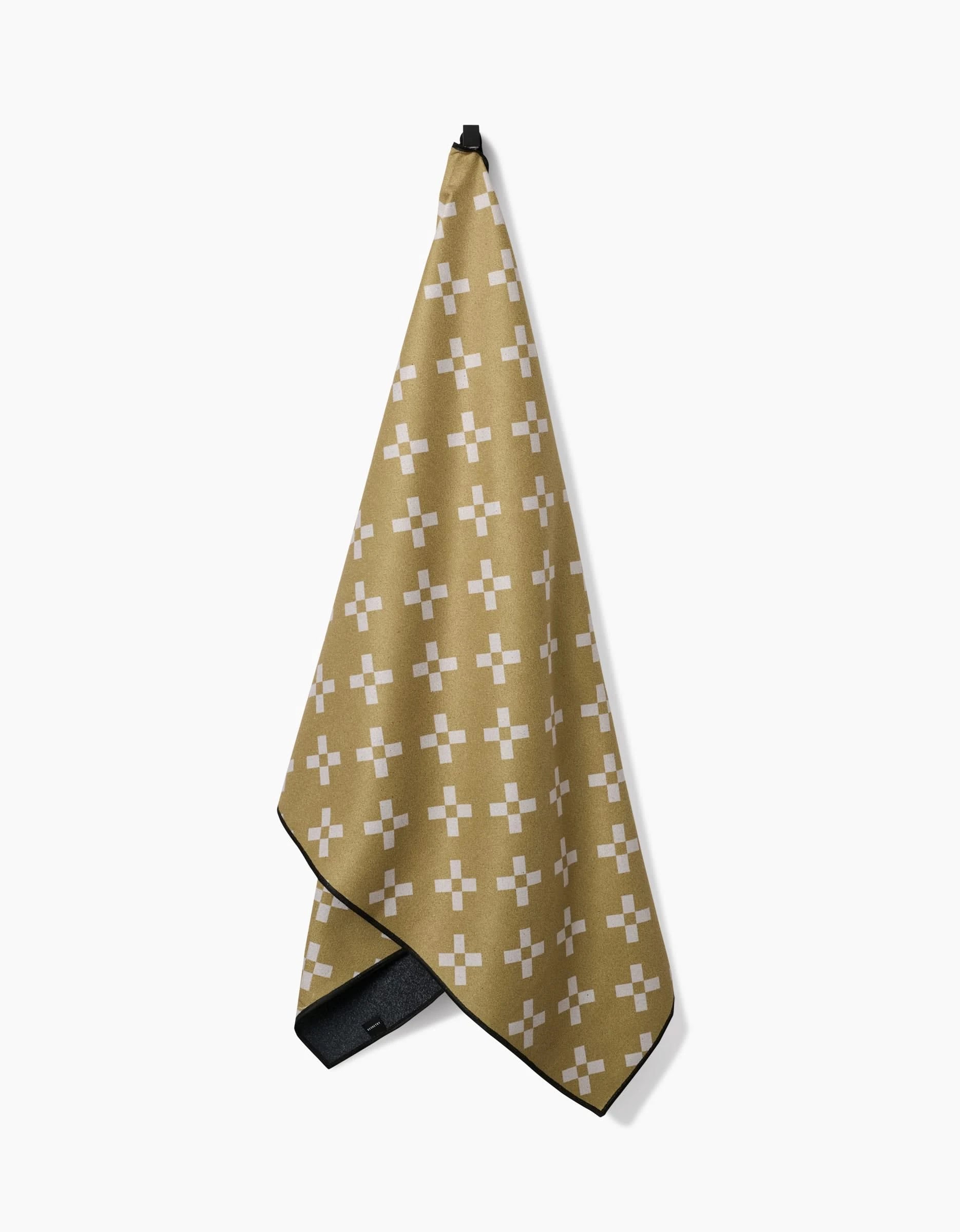 The Lina towel by Anna Christian is tan, quick-drying, and features a white cross pattern. It hangs from a black loop against a plain white background.