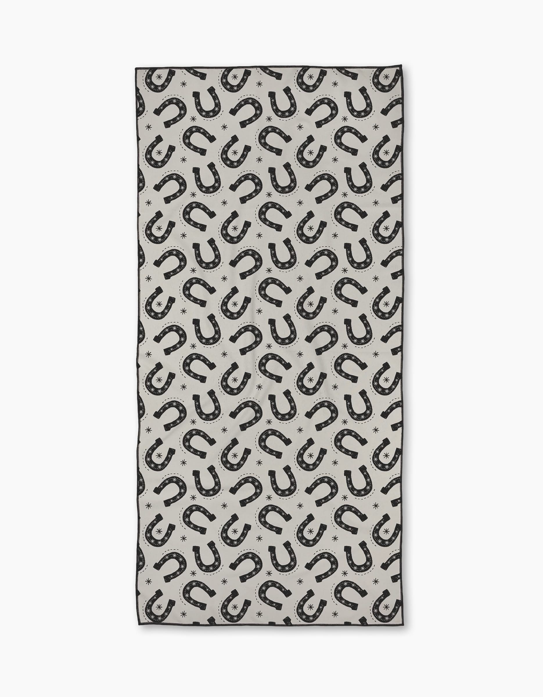 The Geometry Lucky Stride Micro-loop Beach Towel features a repeating black horseshoe and small star pattern on light gray. Made from recycled materials, this quick-drying rectangular towel shows horseshoes in various directions.