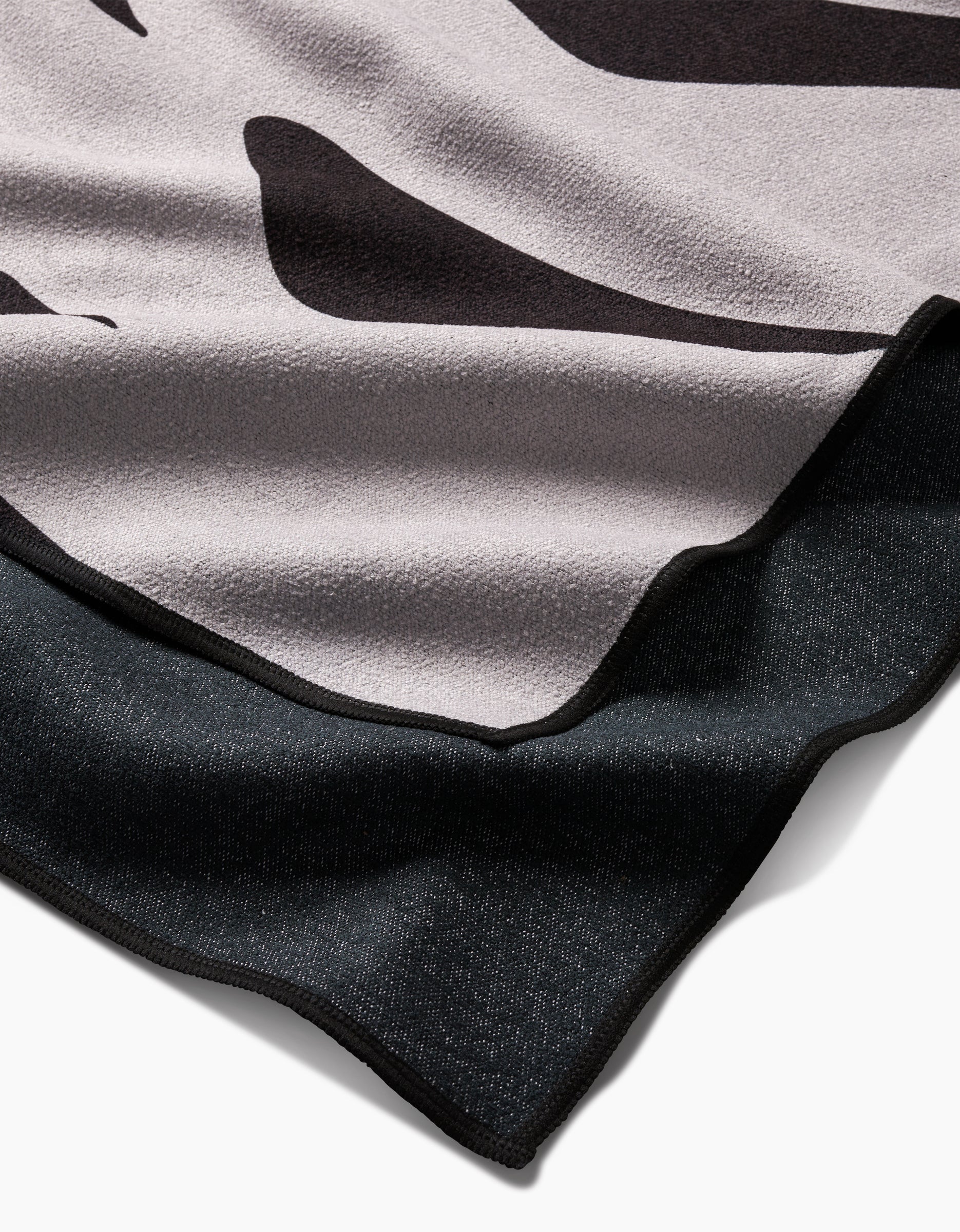 A close-up of the Monstera by PrintedPlant highlights its soft, quick-drying fabric with a black and light gray abstract pattern and neatly finished edges. The folded edge reveals both sides of this stylish beach towel.