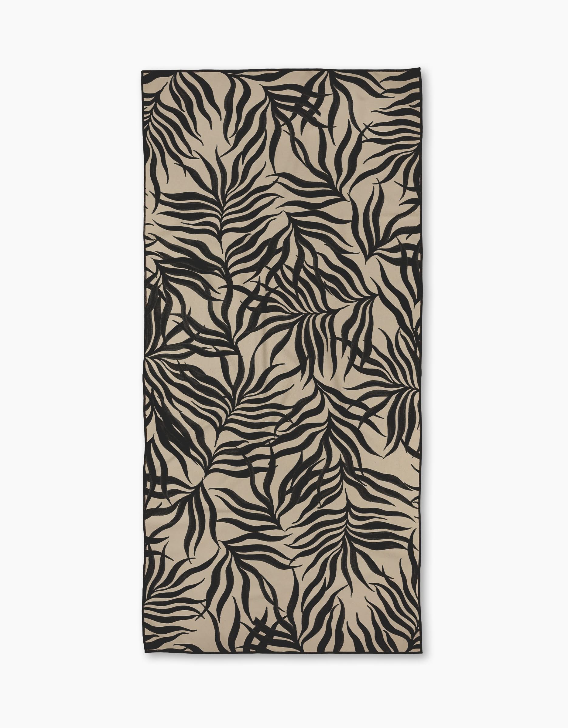 The Geometry Solar Flare Micro-loop Beach Towel features a rectangular beige design with black abstract tropical leaf patterns on white, made from quick-drying recycled materials.