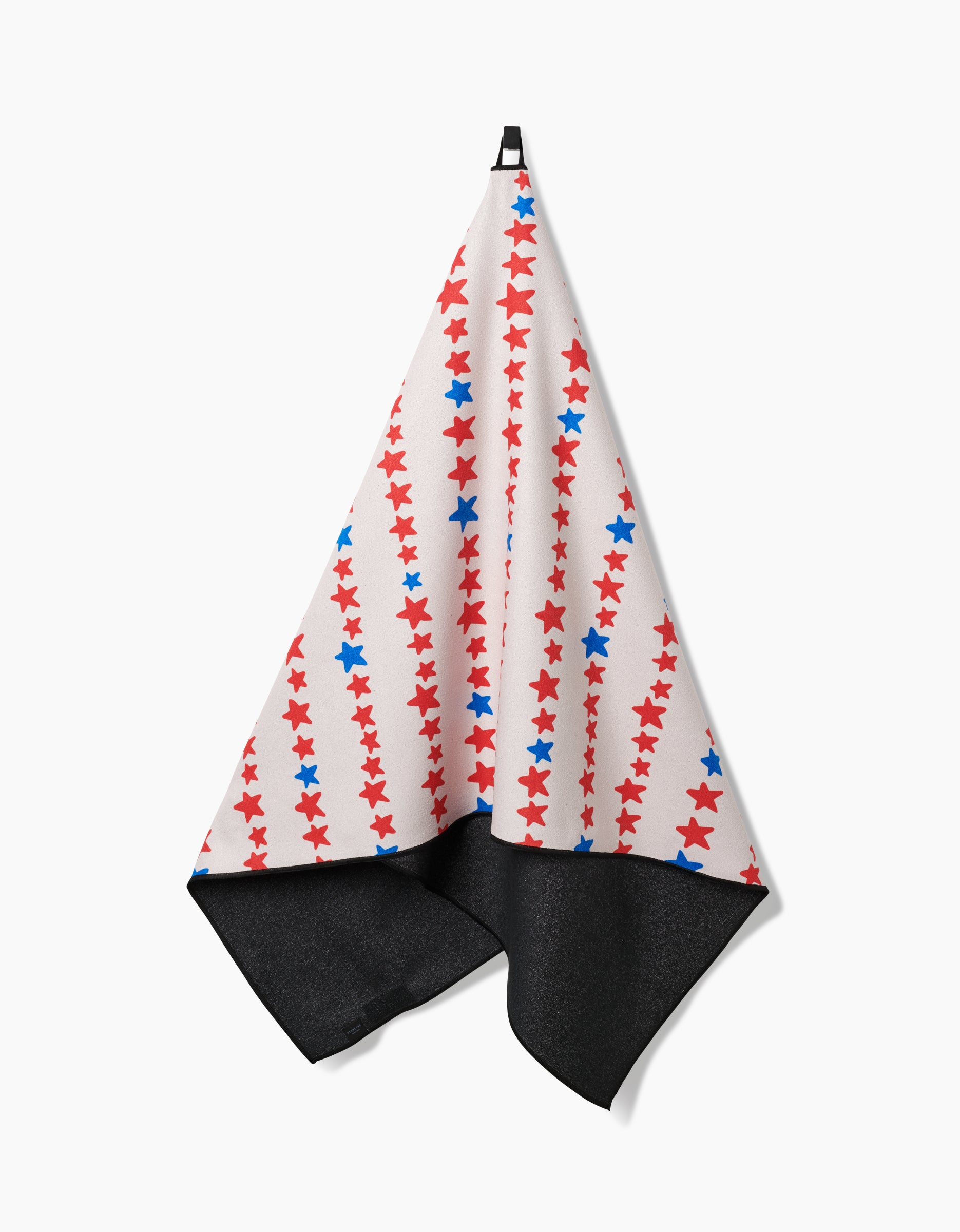 The Starry Stripes beach towel by Kayla Ann hangs on a hook, displaying its quick-drying micro-loop fabric with red and blue stars on a white background and a dark gray underside.