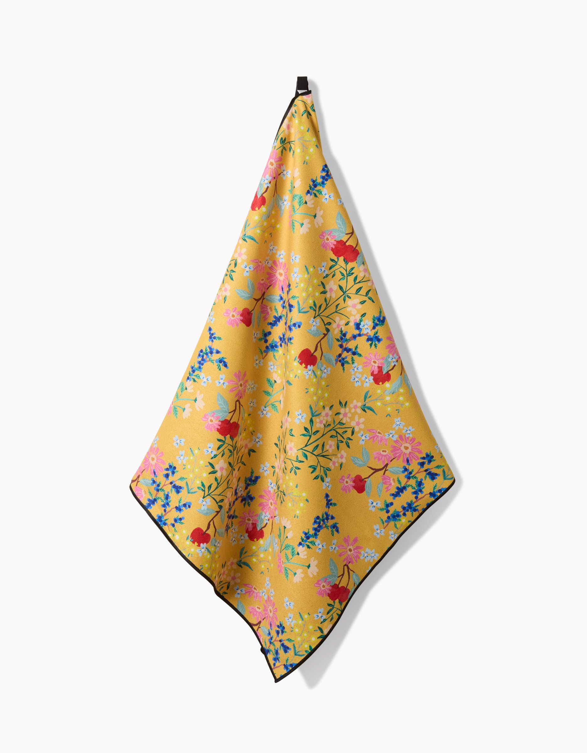 The Sunny Cherry Blossoms towel by Brittany Jepsen, featuring a yellow background with red, pink, blue, and green floral patterns, hangs from a black loop against a plain white backdrop.