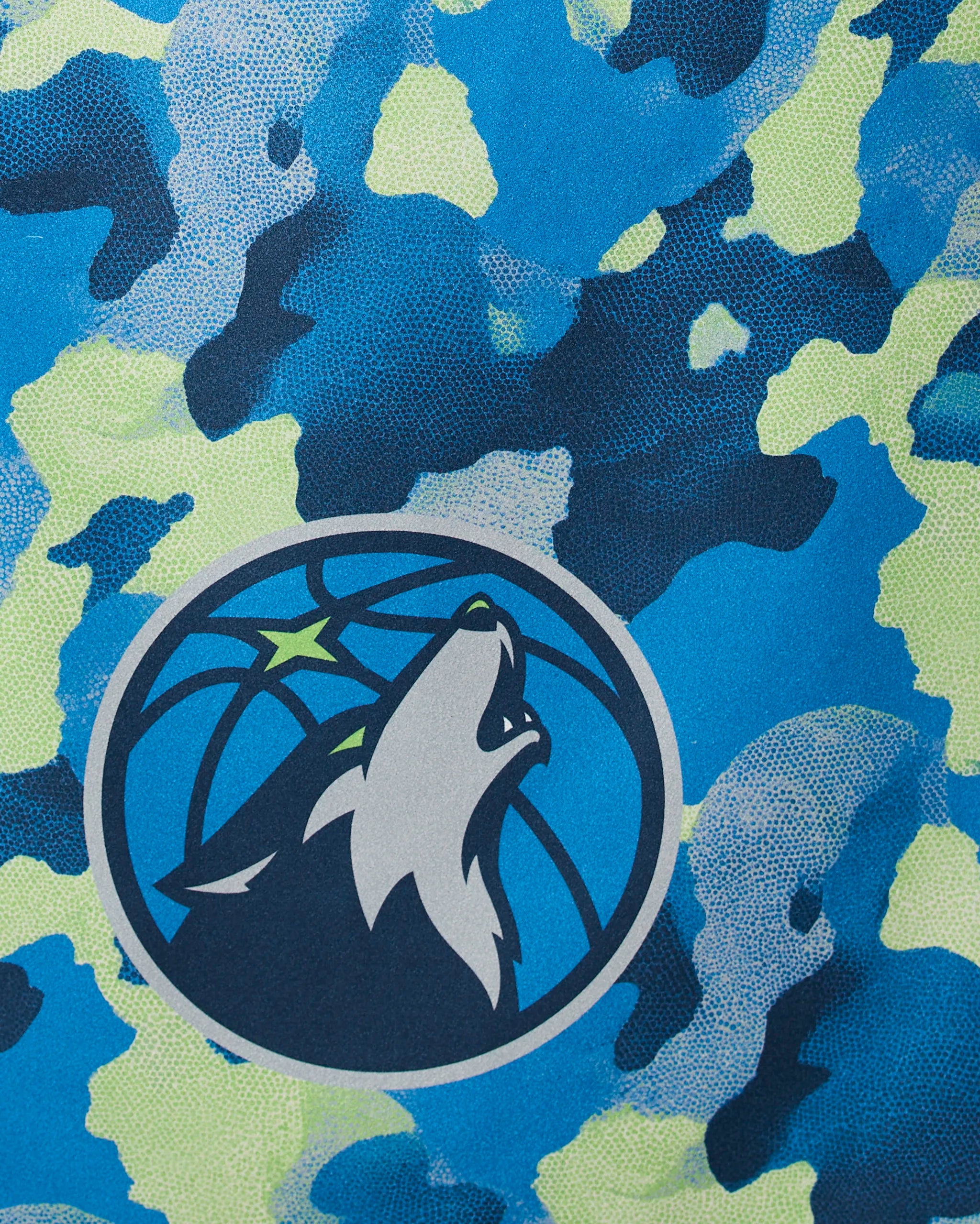 The Geometry Timberwolves Camo features a blue and green camouflage pattern with a circular logo of a howling wolf in front of a stylized basketball and star.