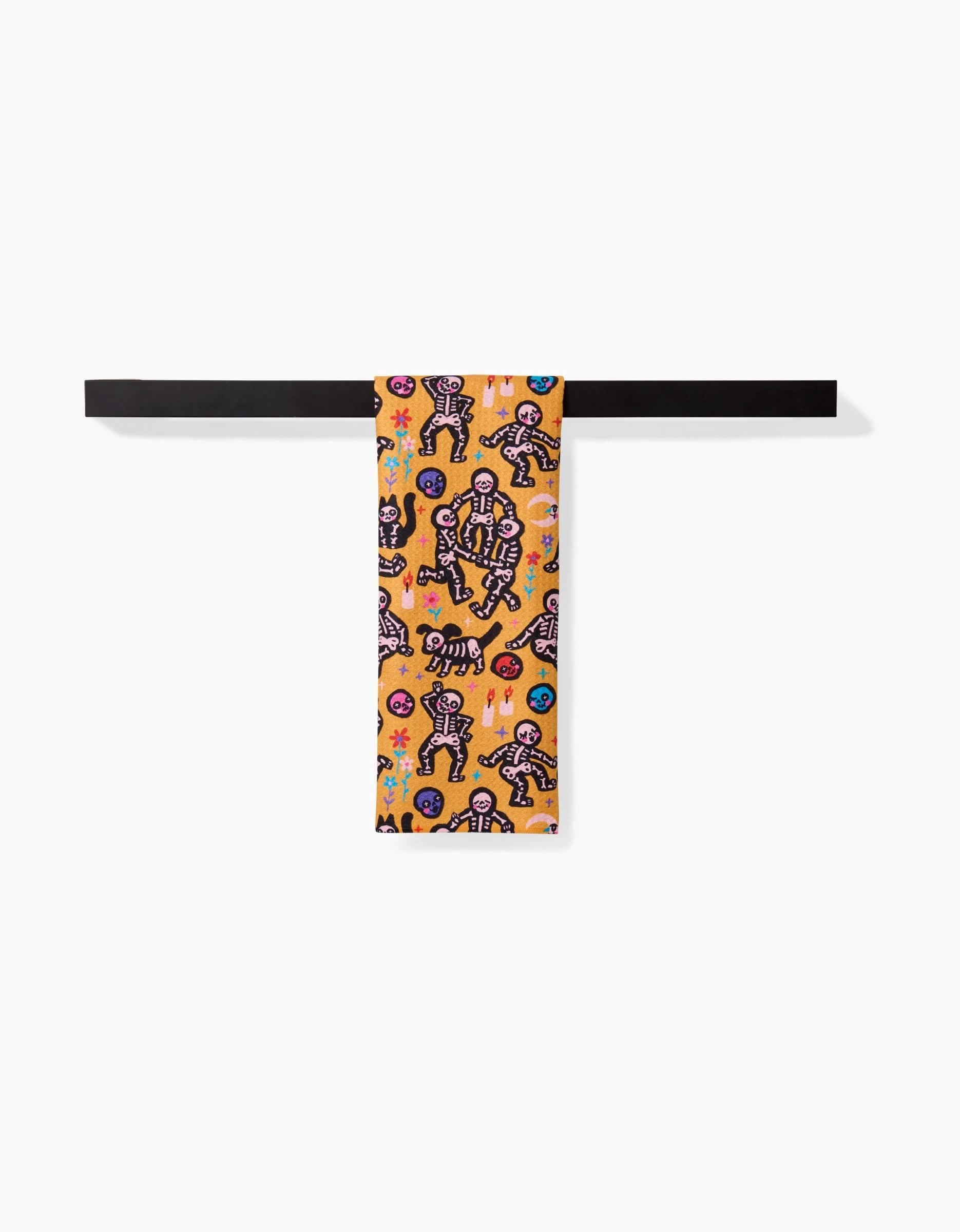 The After Party scarf by So Lazo is made from recycled materials and features cartoon skeletons and flowers on a vibrant orange background, displayed draped over a black bar against a white backdrop.