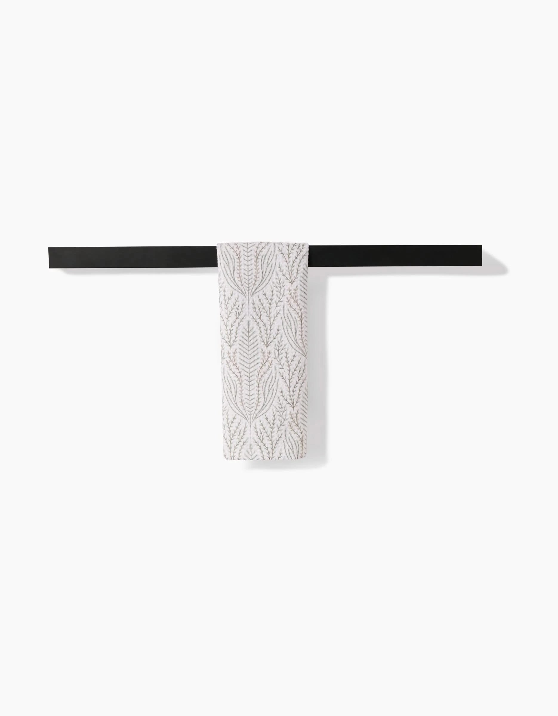 The Amberlin bar towel by Amy MacCready, featuring a subtle leaf pattern and made from ultra-absorbent recycled materials, hangs on a minimalist black towel bar against a white wall.