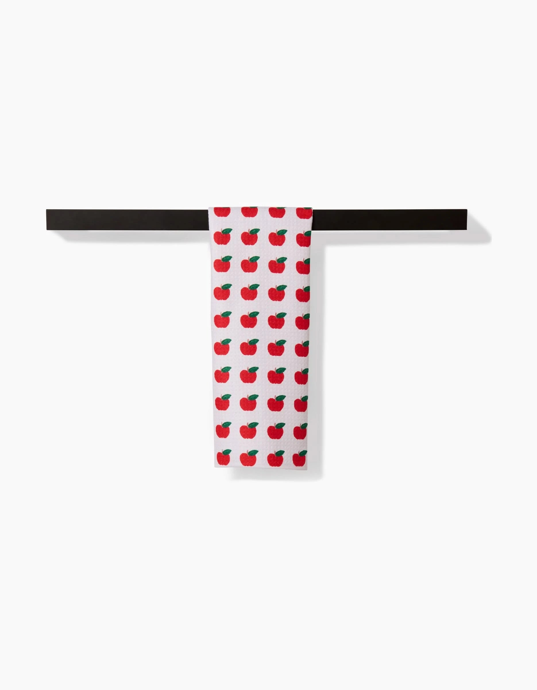 The Apple Grove bar towel by Brittany Jepsen, featuring a red apple pattern on white Geoweave fabric, is draped over a black bar against a plain white background.
